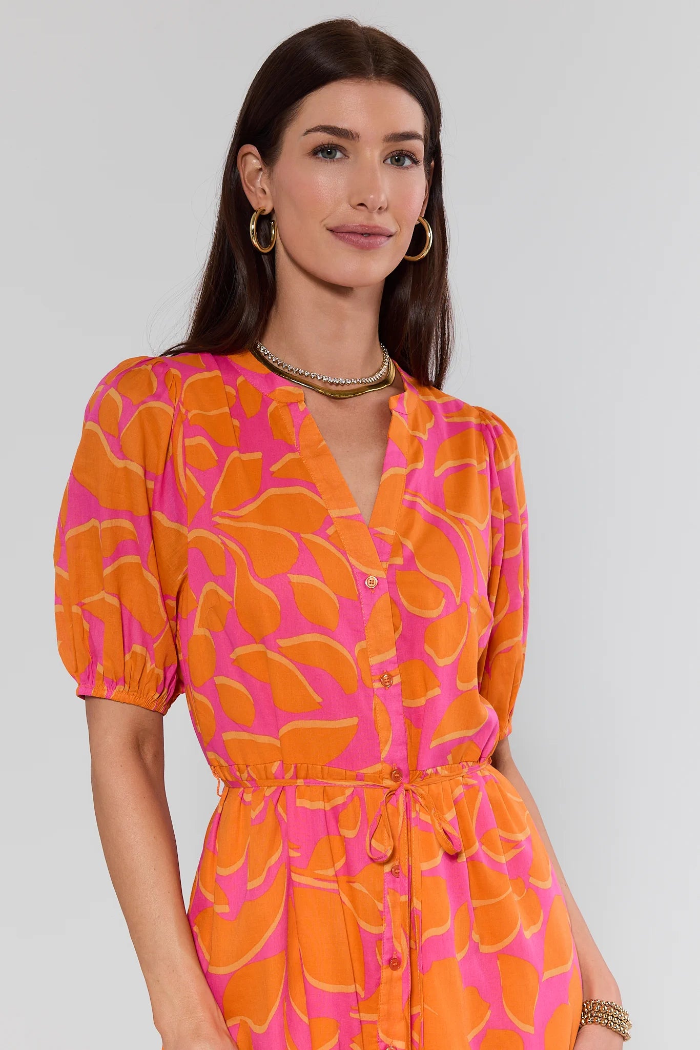 Woman wearing a vibrant orange and pink patterned dress against a plain background