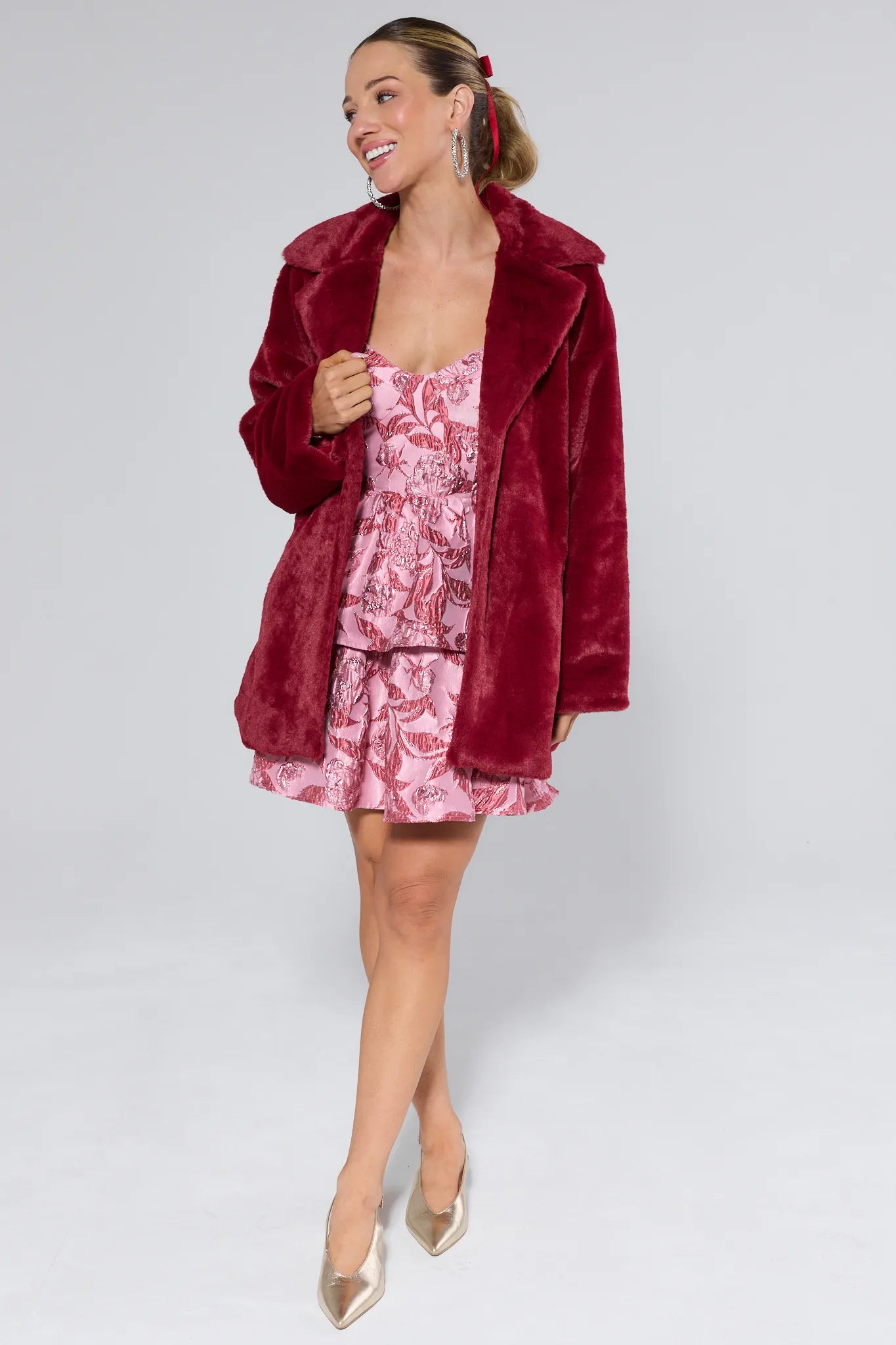 Woman wearing a red velvet coat over a pink floral dress on a white background
