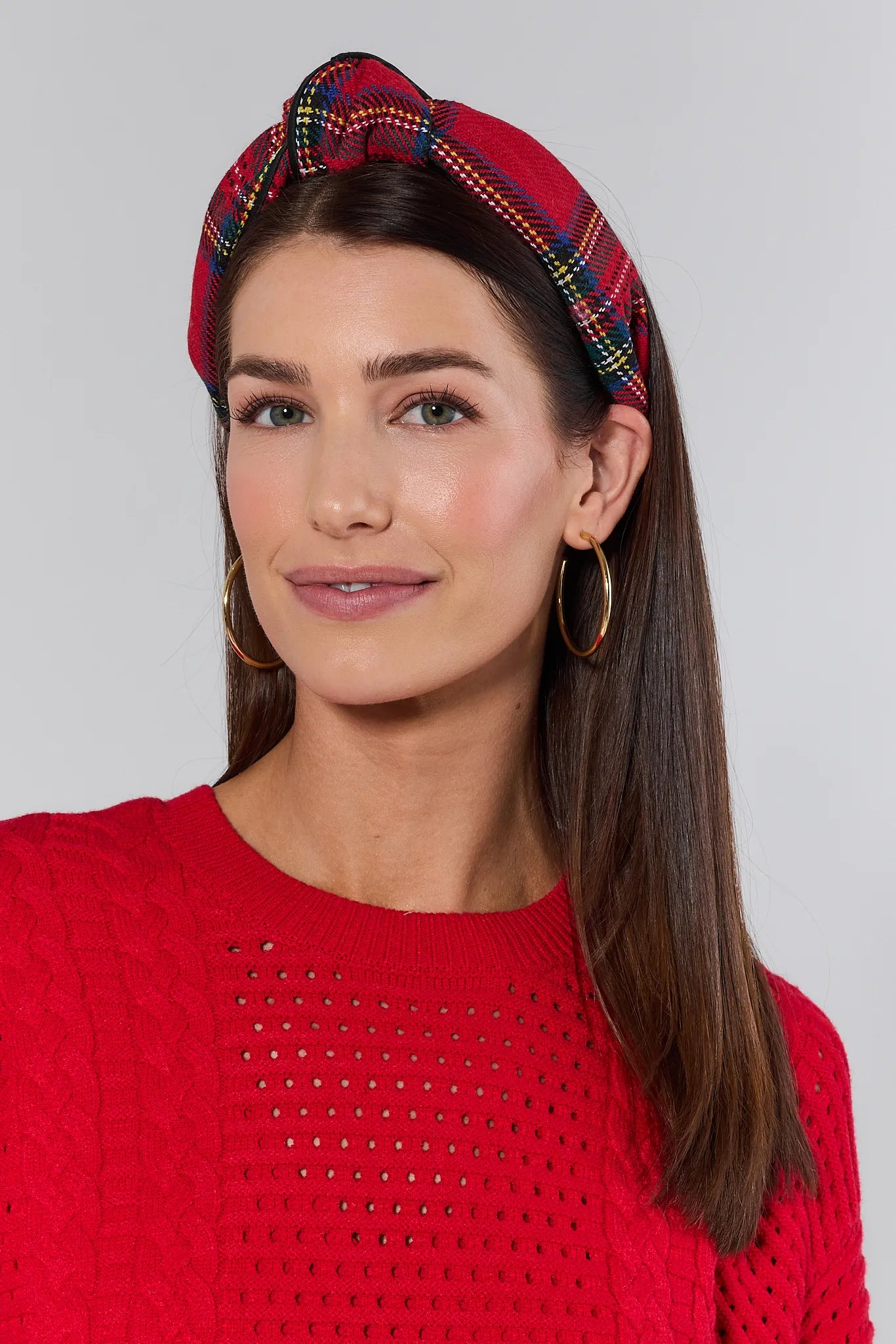 Woman wearing a red knitted sweater and Holly Plaid Headband against a plain background