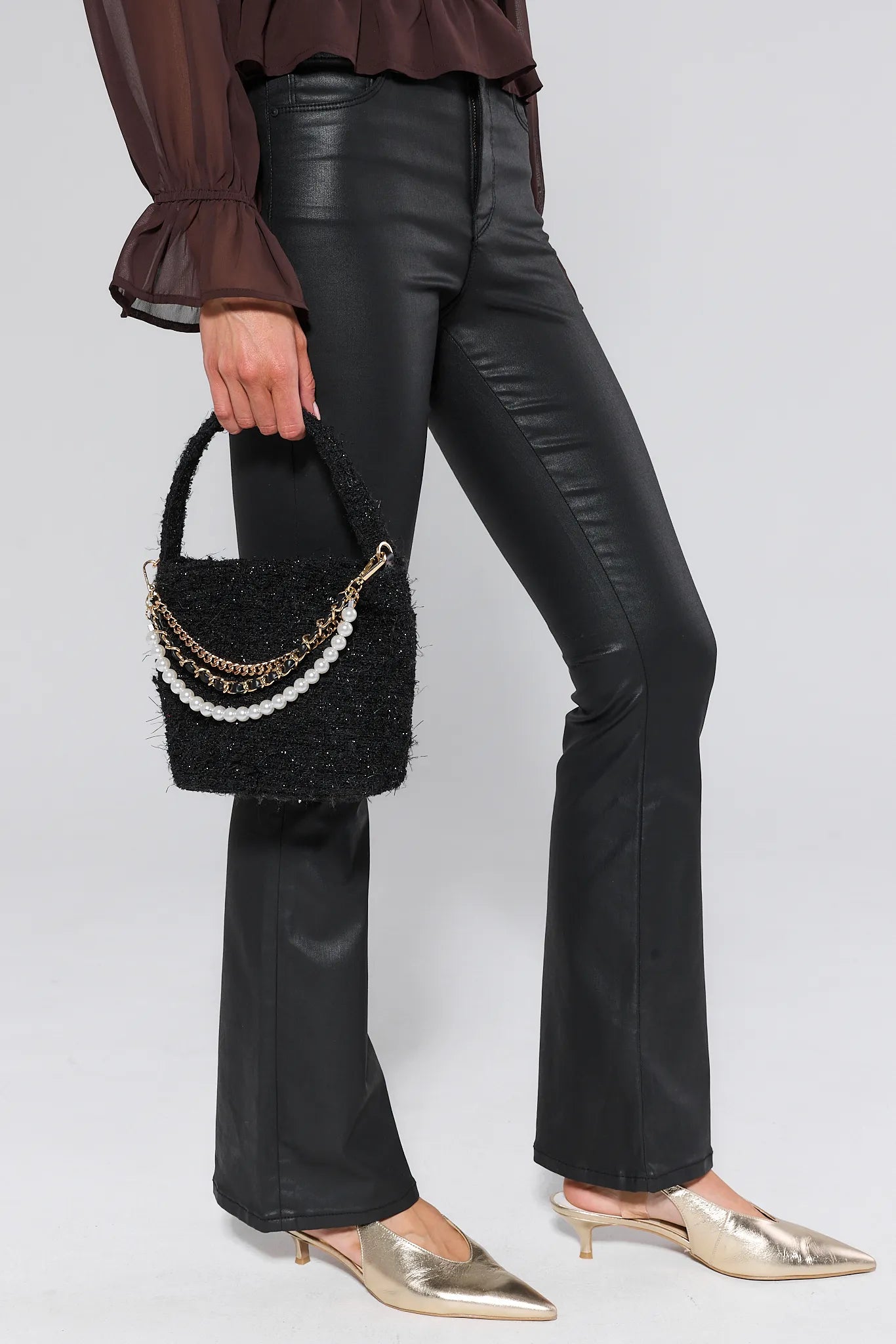 Person wearing black leather pants holding a Chloe Black Tweed Bag with pearl and chain details on a white background