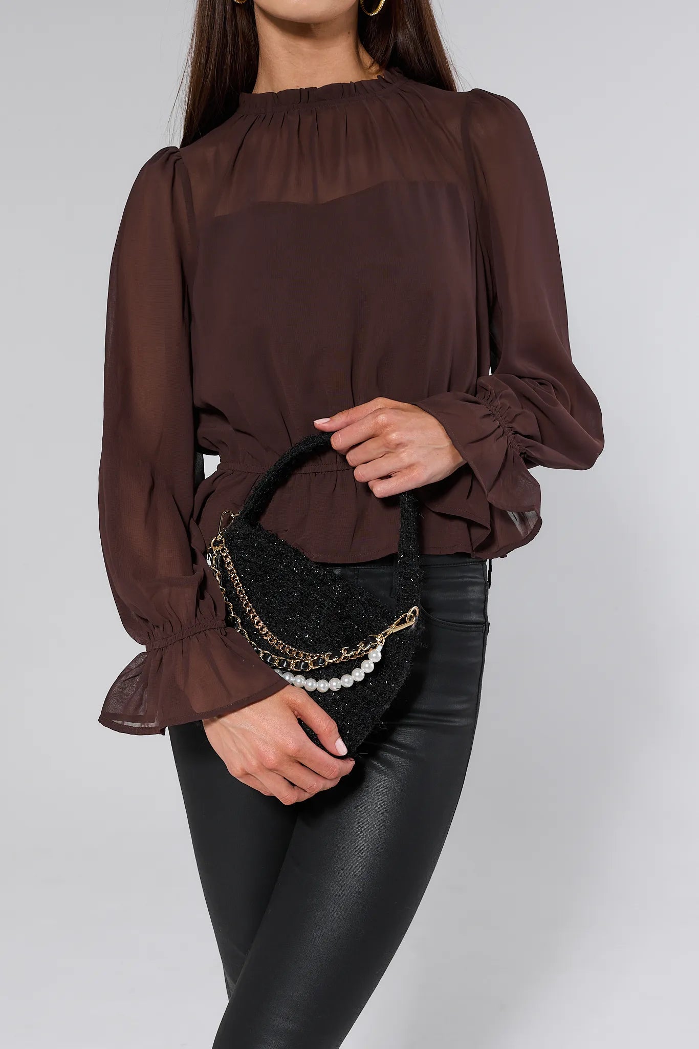 Person wearing black leather pants holding a Chloe Black Tweed Bag with pearl and chain details on a white background