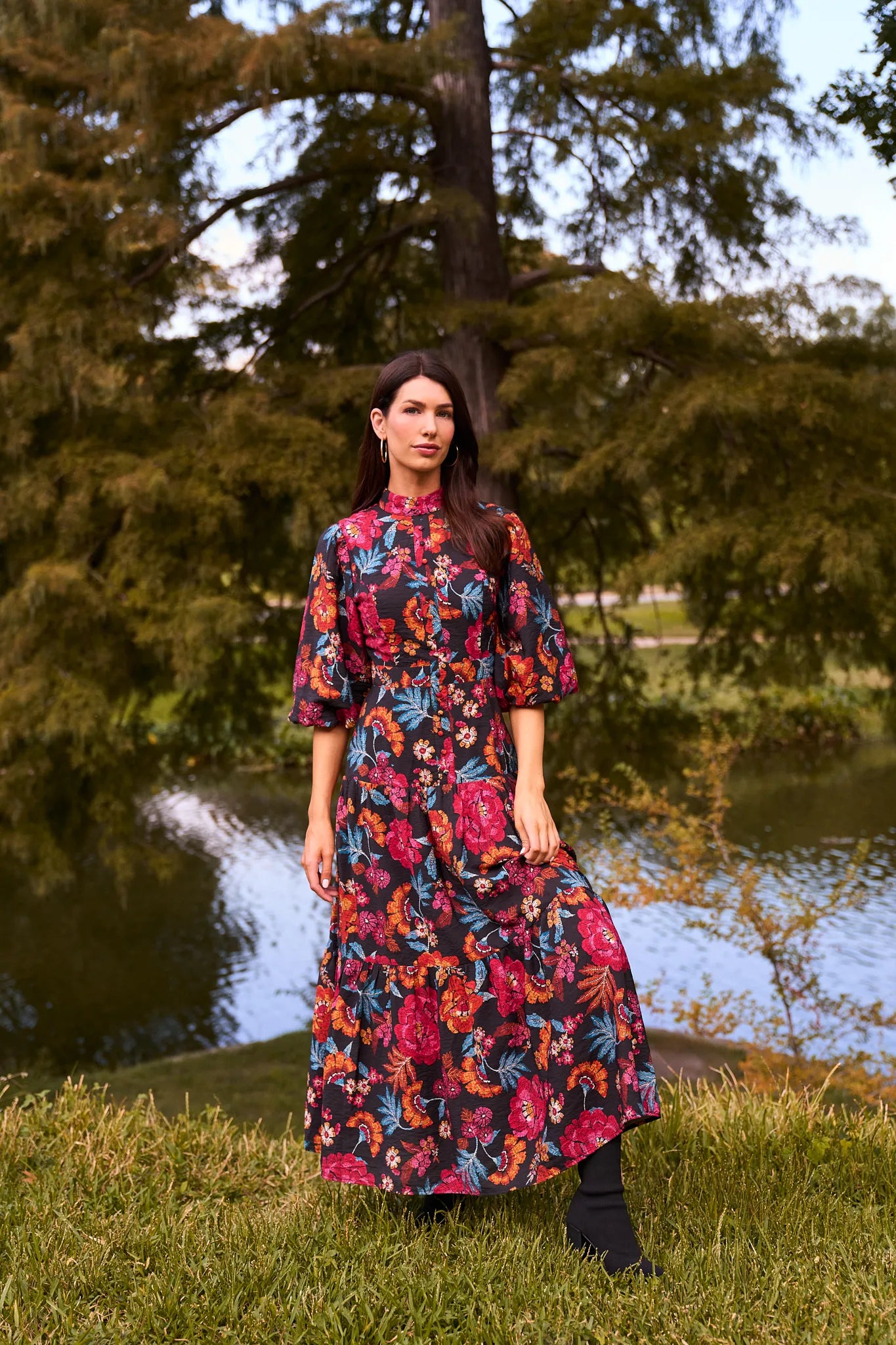 Woman in a floral Desi Dress
 standing by a pond with trees in the background