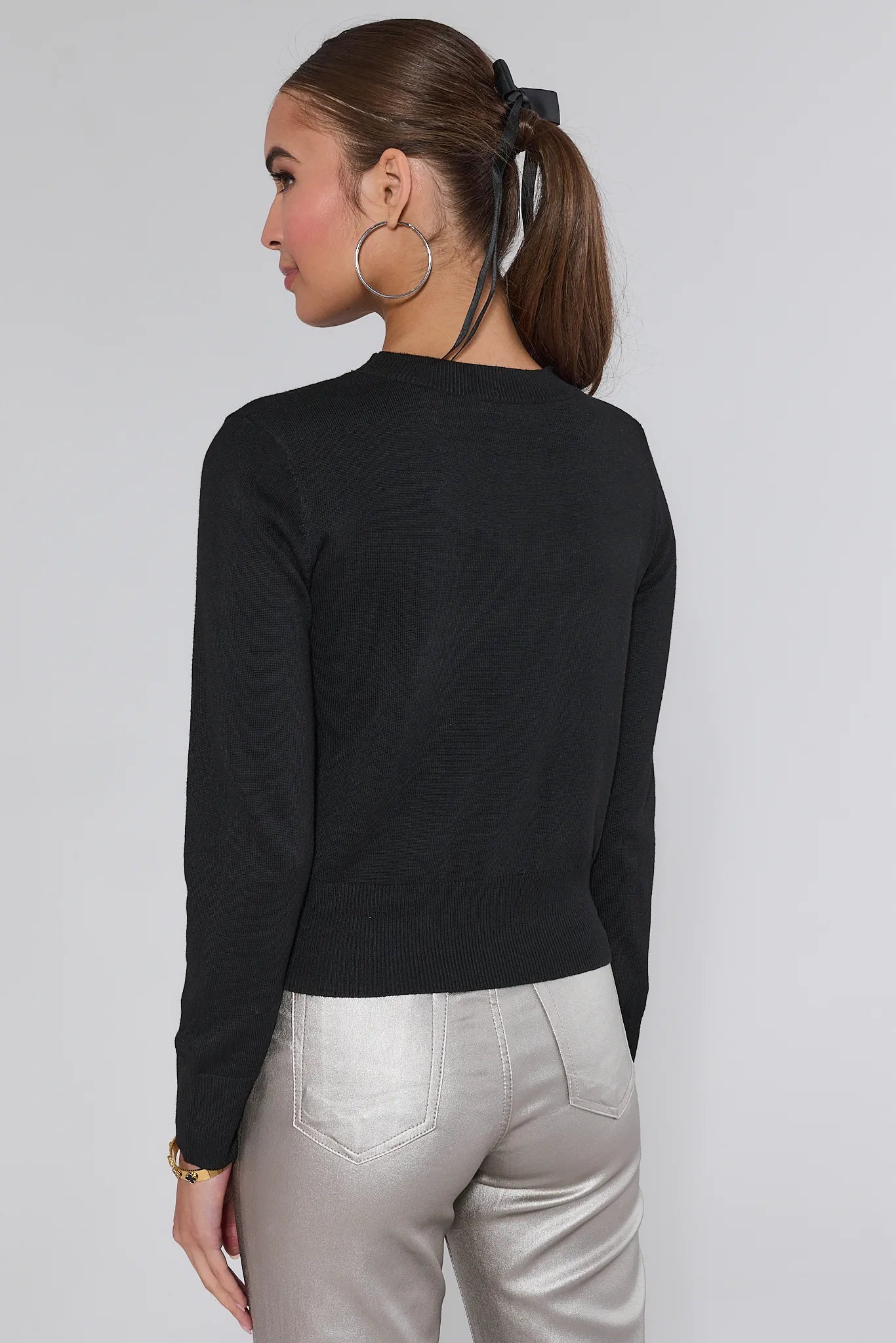Woman wearing a Ainsley Black Embellished Knit Sweater and silver pants on a white background