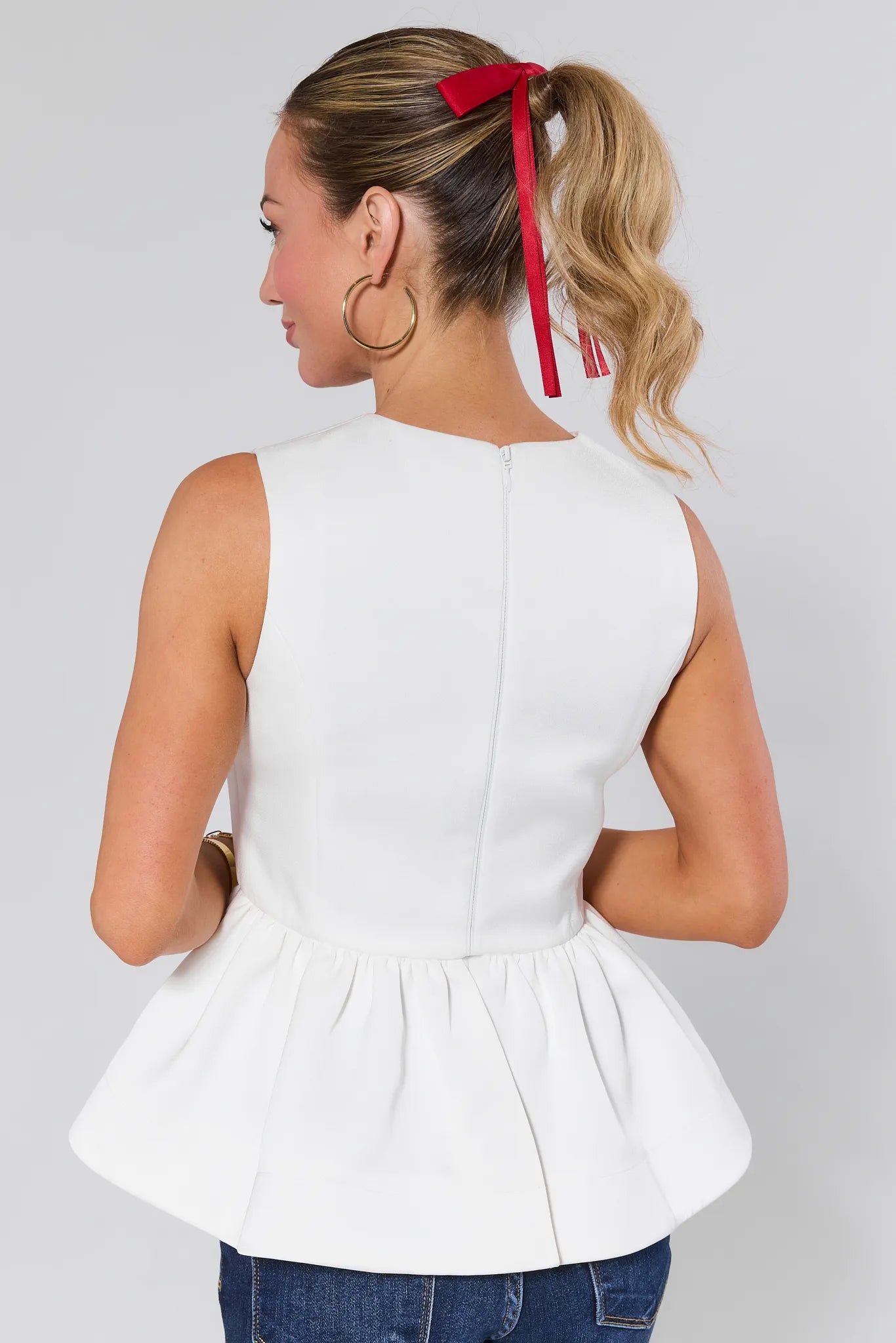 Woman wearing a Blakey Ivory Peplum Top and blue jeans against a plain background