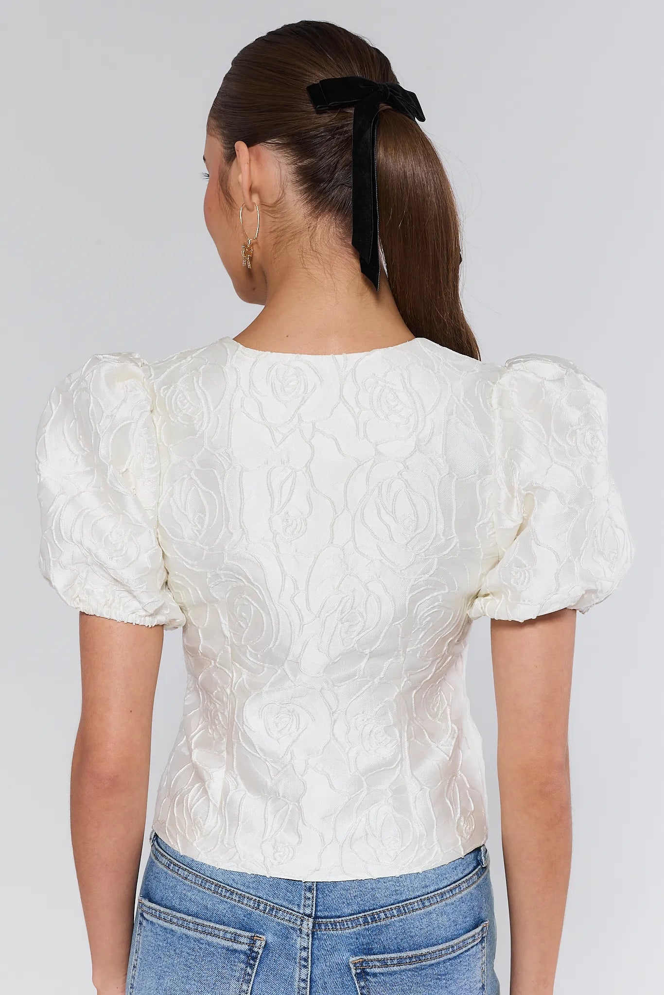 Person wearing a white textured blouse with puffed sleeves and blue jeans on a plain background