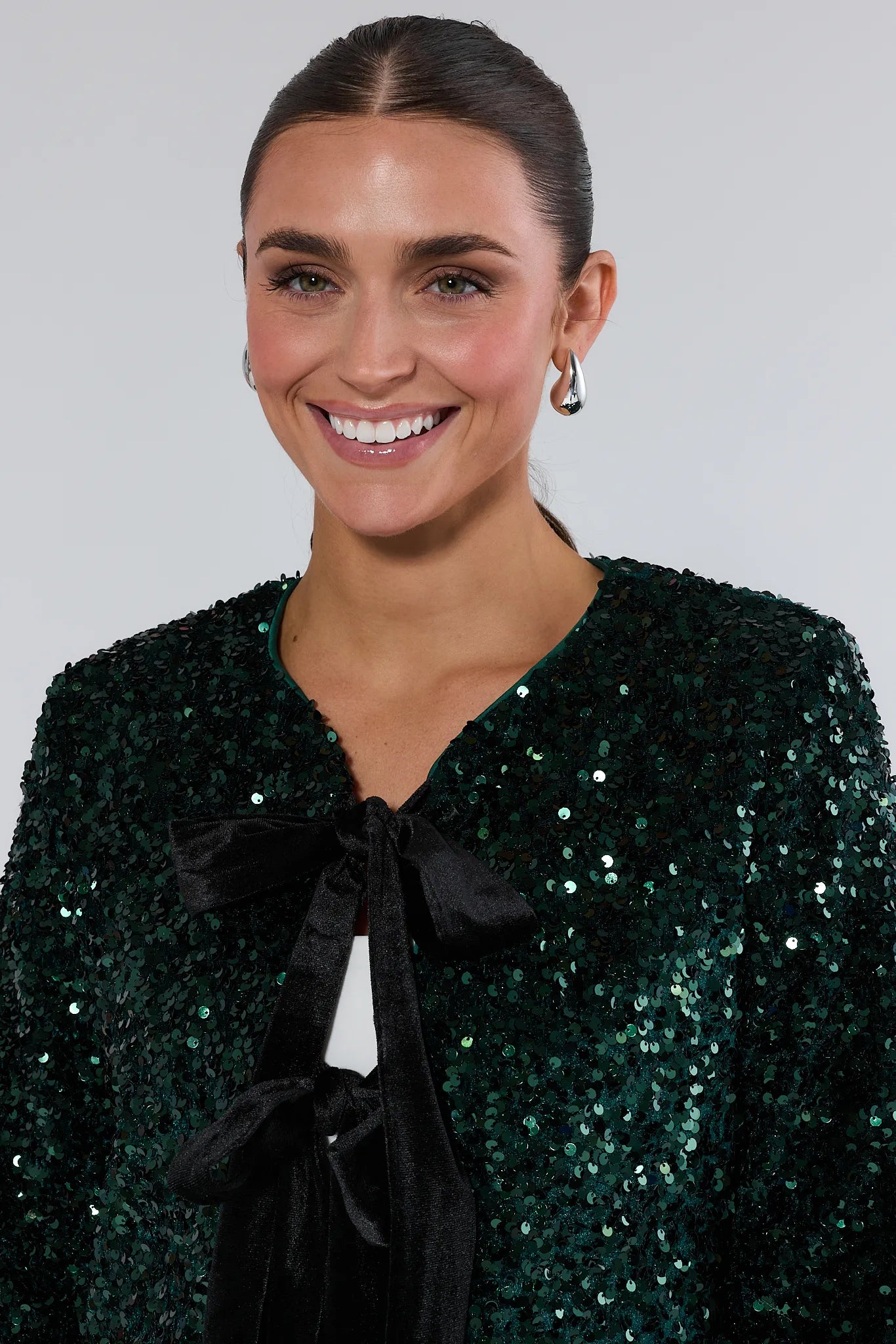 Woman wearing a green sequin ashley jacket with a black bow tie against a plain background