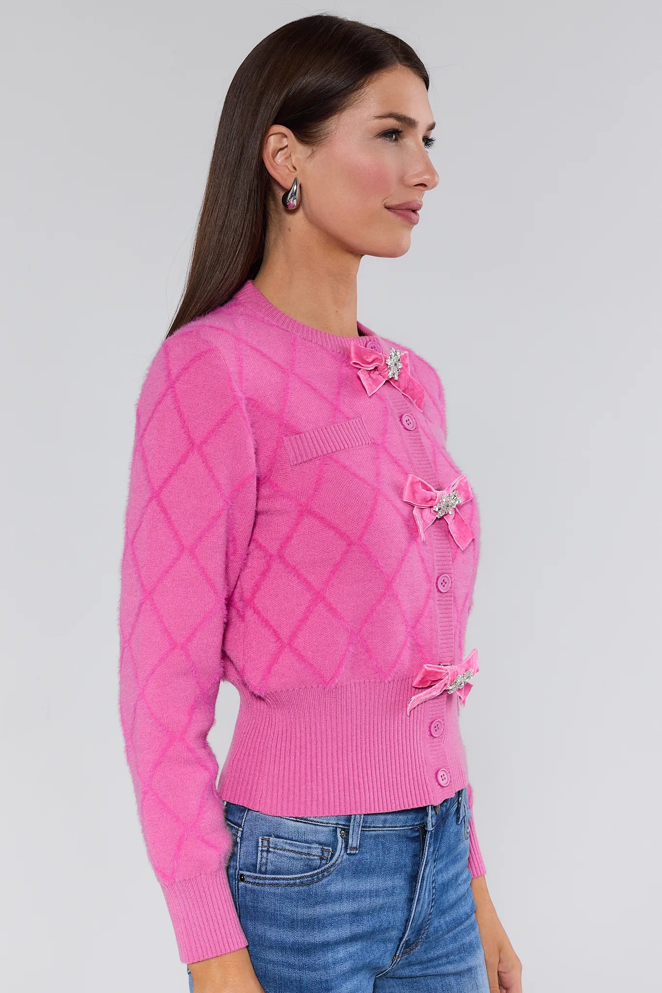 Woman wearing a Emily Pink Bow Cardigan with decorative bows and buttons on a plain background