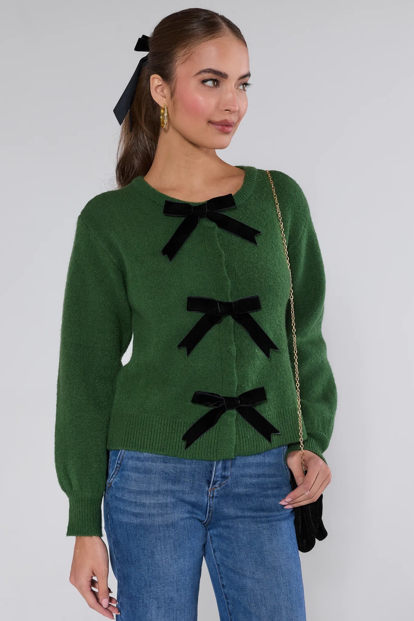 Woman wearing a Everly Green Bow Knit Sweater with black bows and blue jeans against a white background