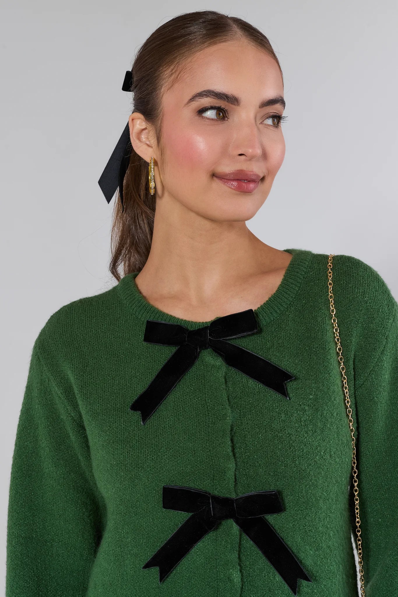 Woman wearing a Everly Green Bow Knit Sweater with black bows and blue jeans against a white background