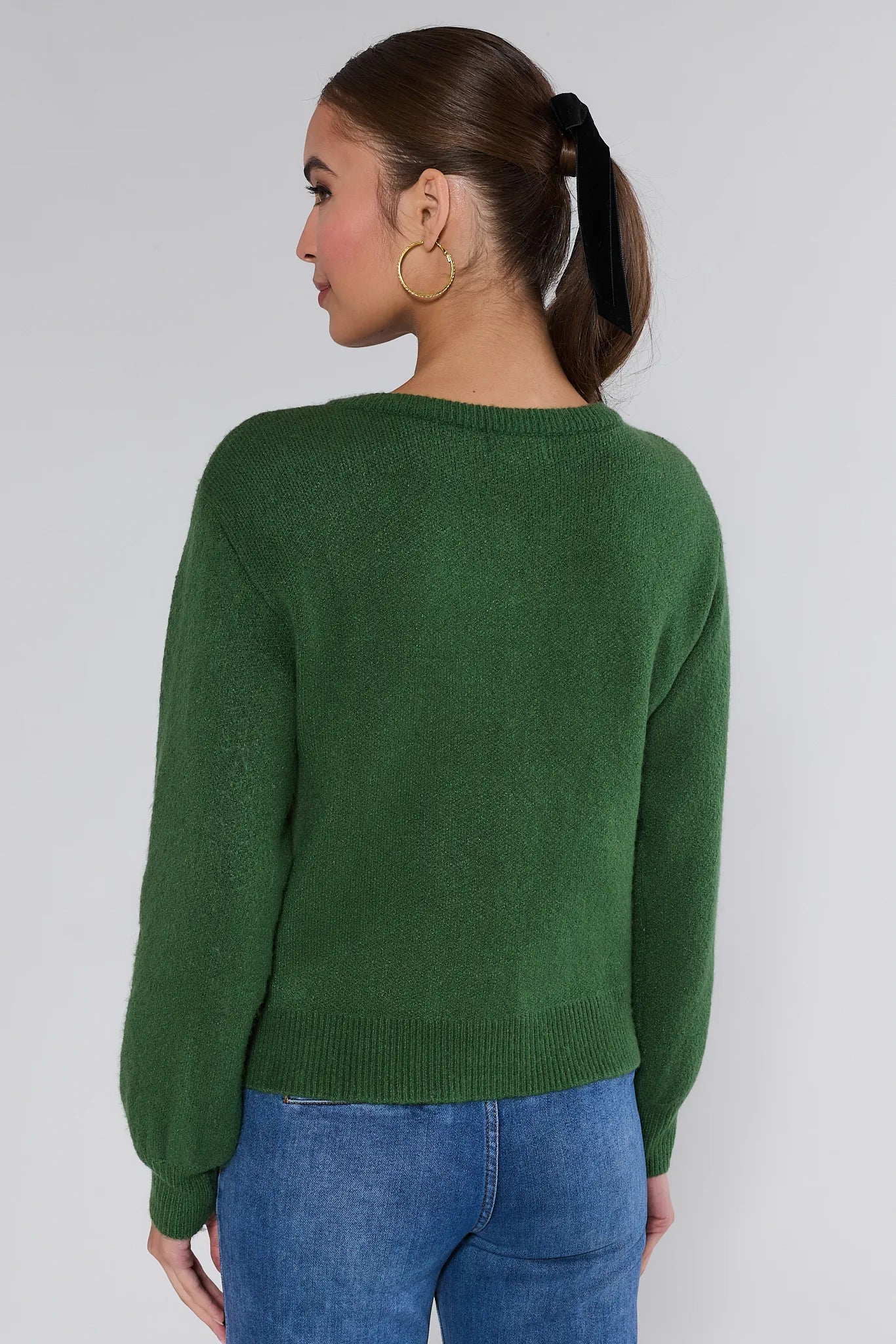 Woman wearing a Everly Green Bow Knit Sweater with black bows and blue jeans against a white background