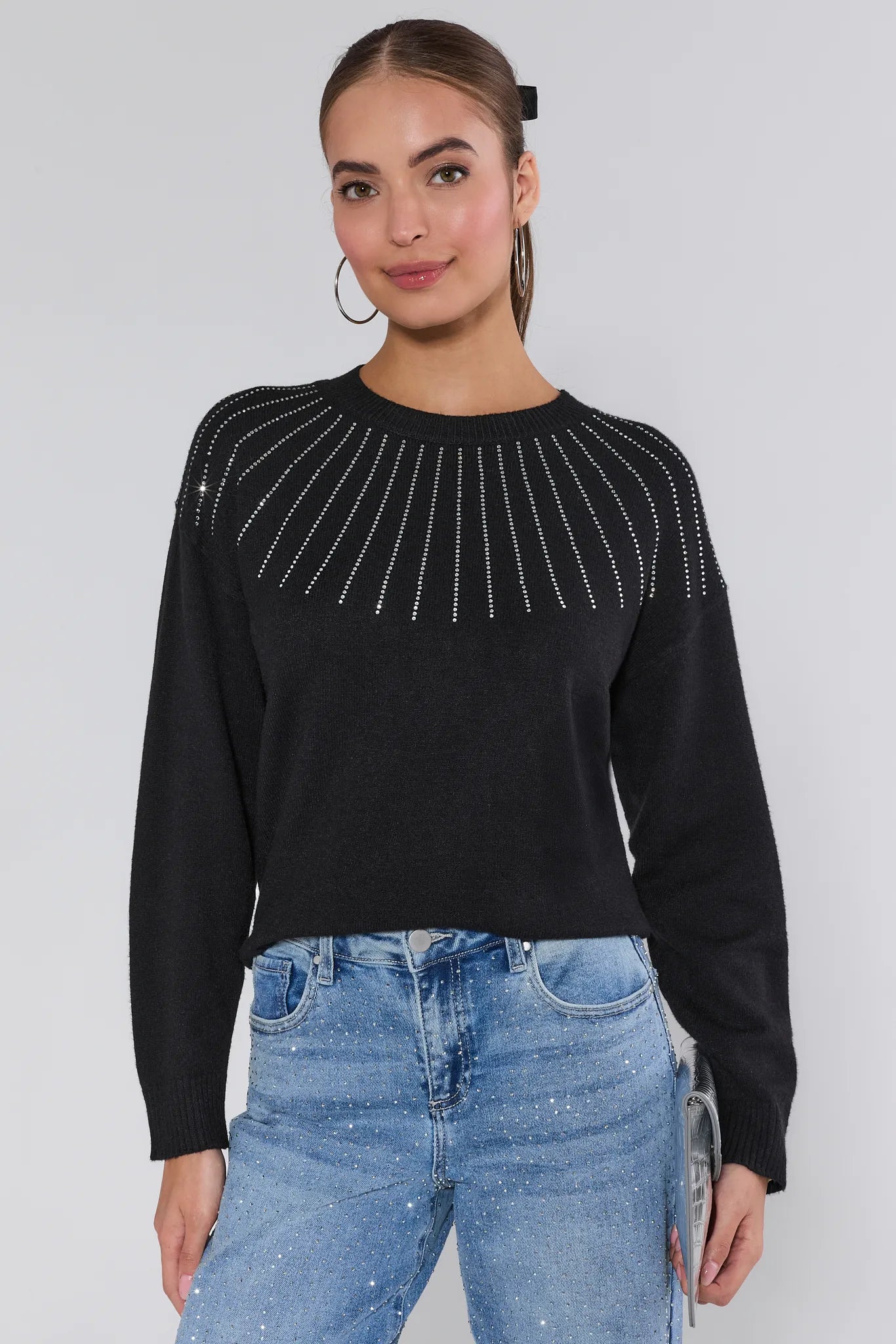 Woman wearing a Sondra Black Embellished Sweater with decorative elements and blue jeans on a white background