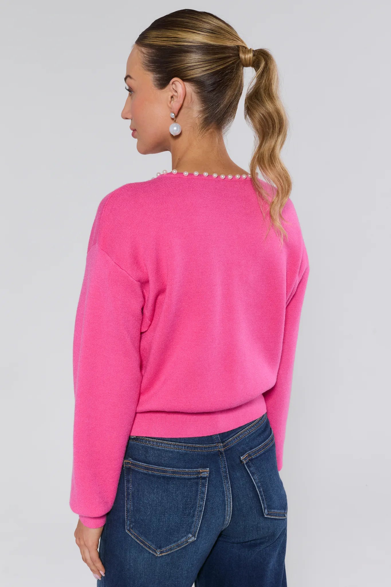 Person wearing a bright pink sweater with pearl trim on a plain background