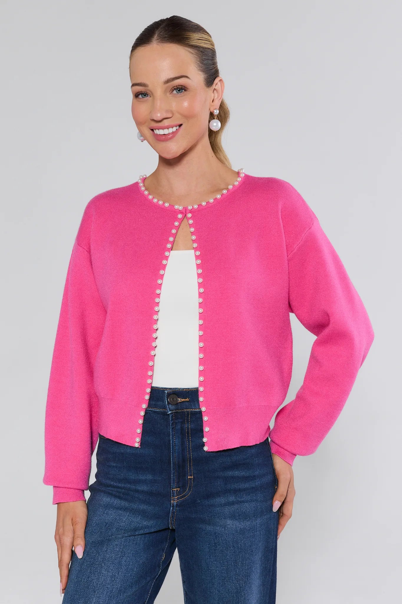 Woman wearing a pink cardigan with pearl buttons on a plain background