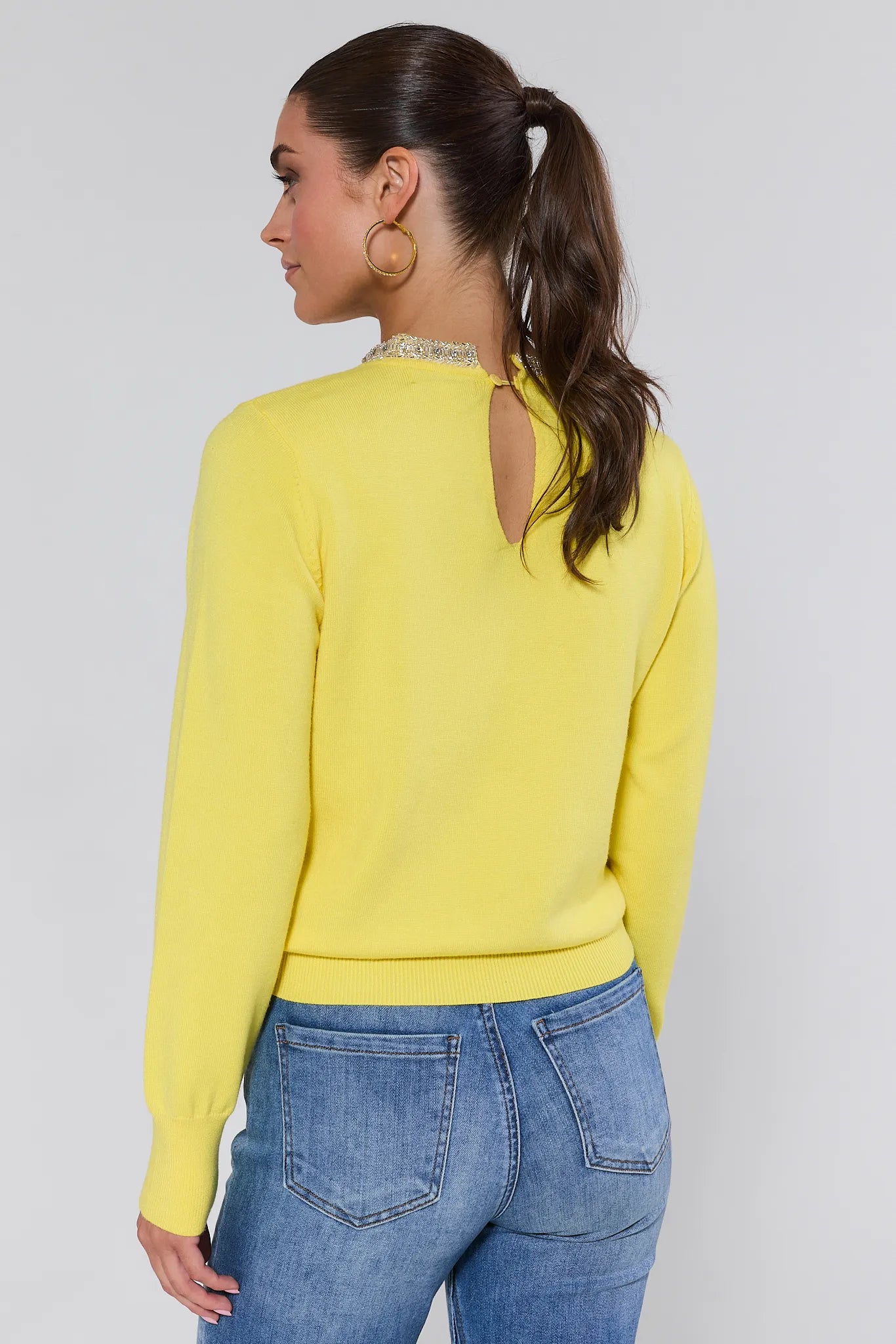 Woman wearing a yellow victoria sweater and blue jeans against a plain background
