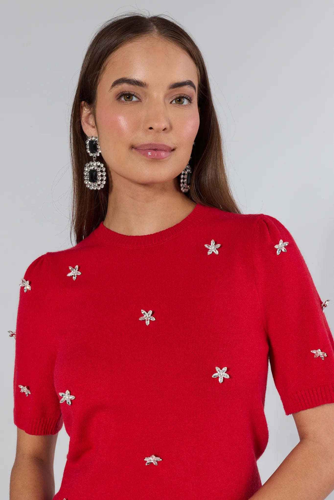 Woman wearing a red sweater with white floral patterns on a plain background