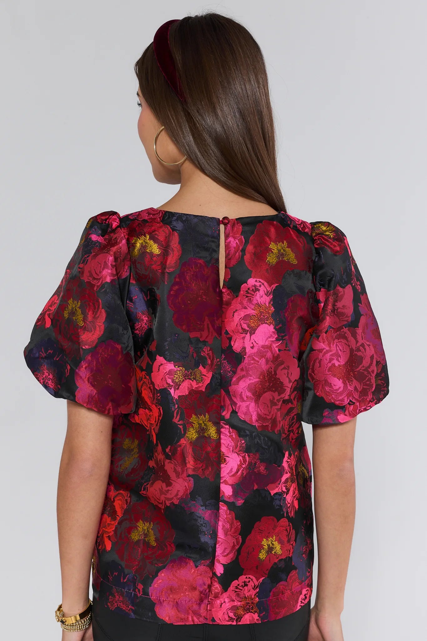 Woman wearing a floral Ruby Top with pink and red flowers on a plain background