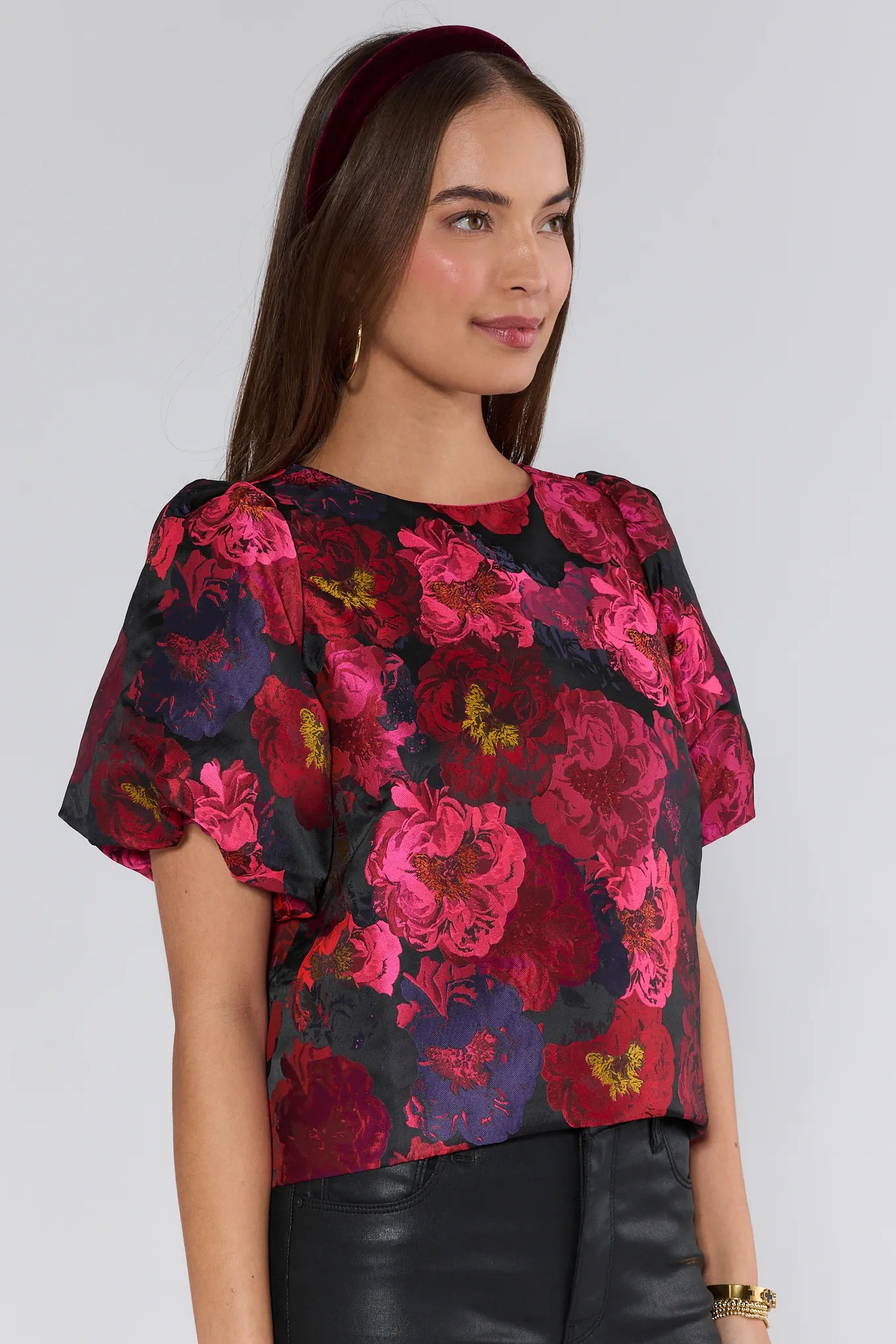 Woman wearing a floral Ruby Top with pink and red flowers on a plain background
