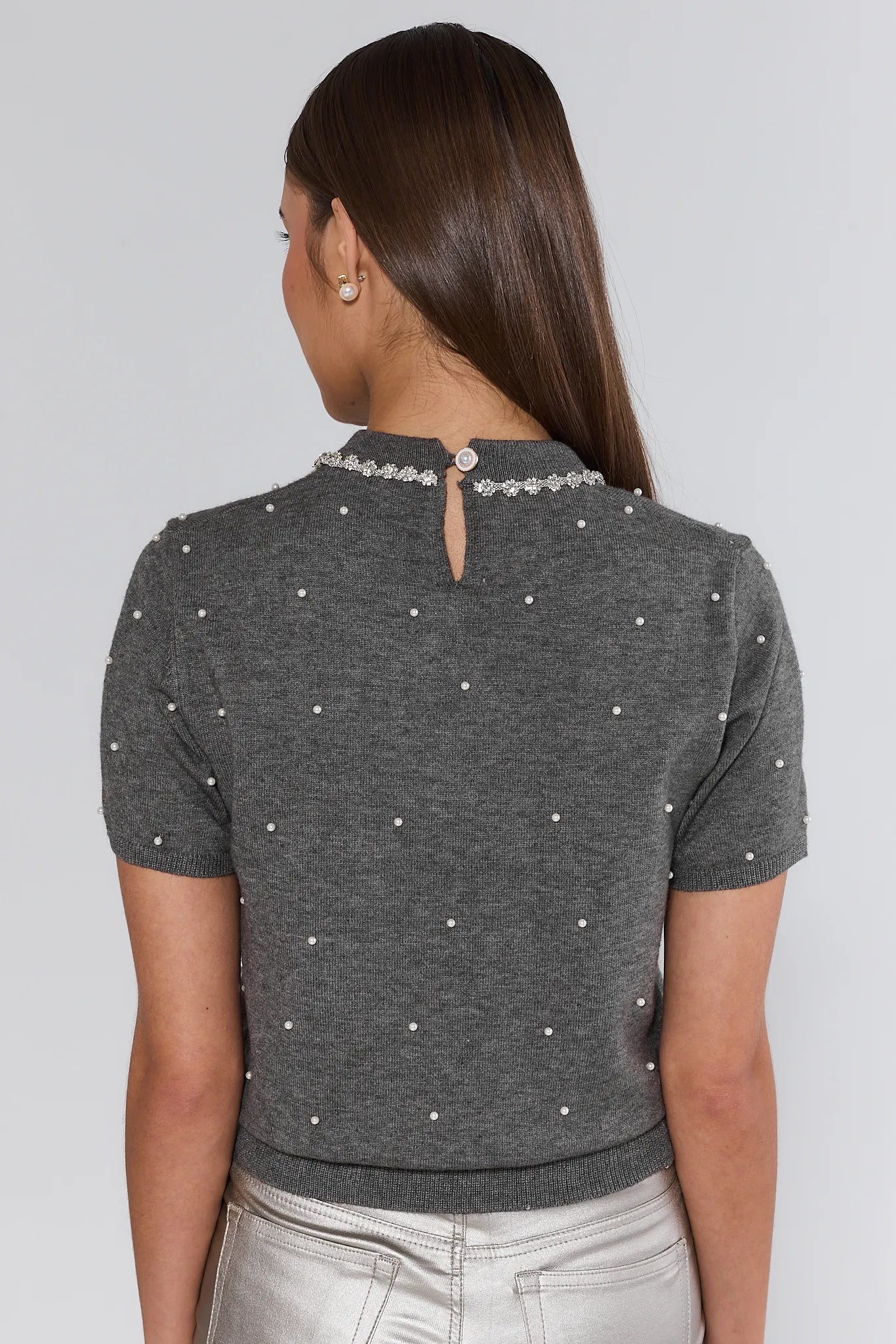 Woman wearing a gray short-sleeve top with pearl embellishments on a plain background