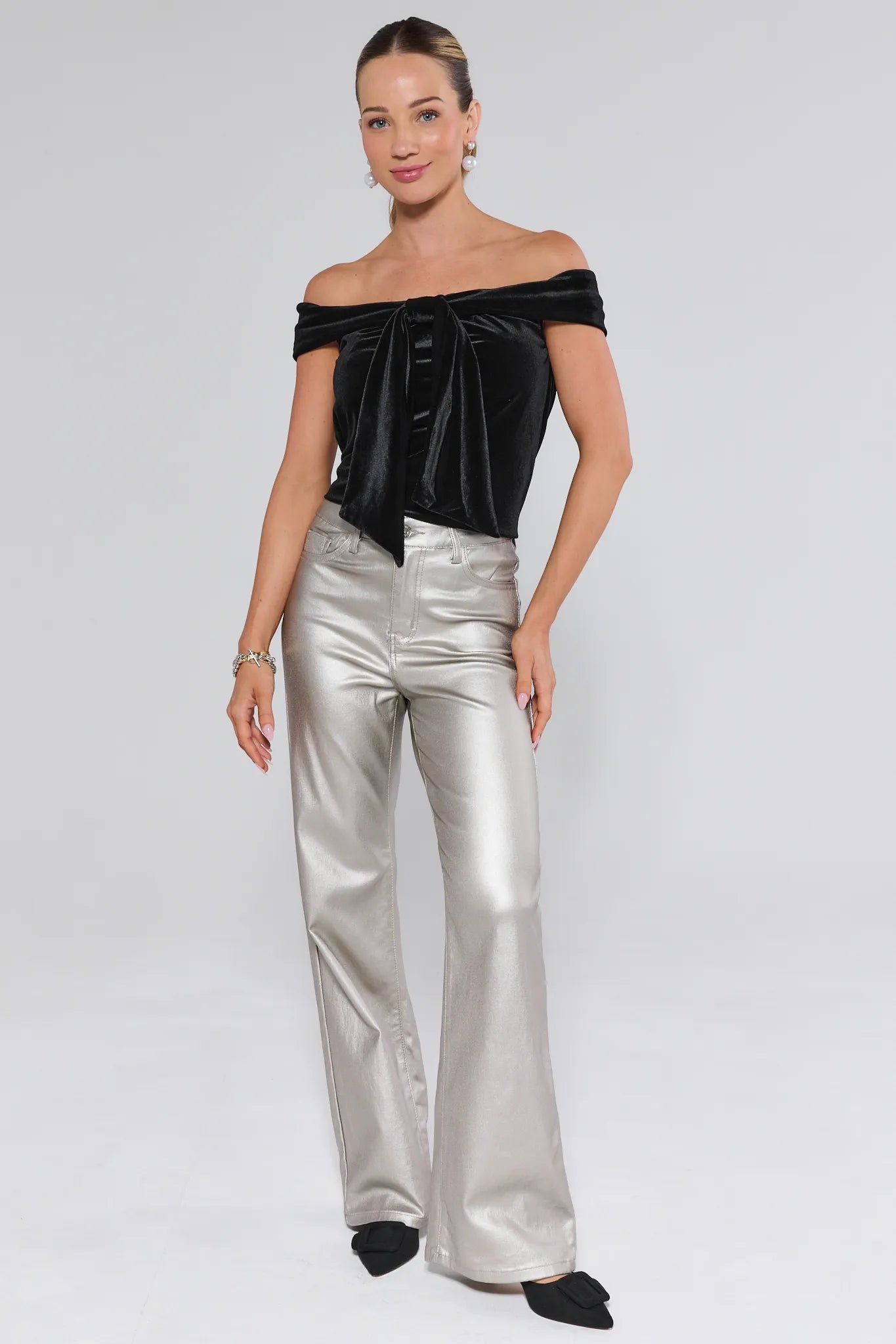 Woman wearing a black off-shoulder top and silver pants on a white background