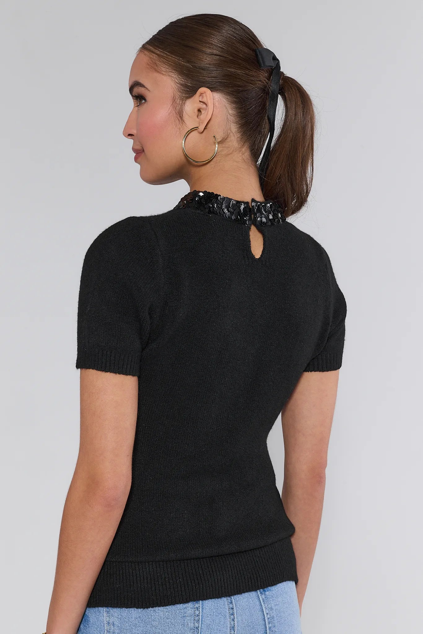 Woman wearing a black short-sleeve Vicki Sweater with a sequin collar against a white background