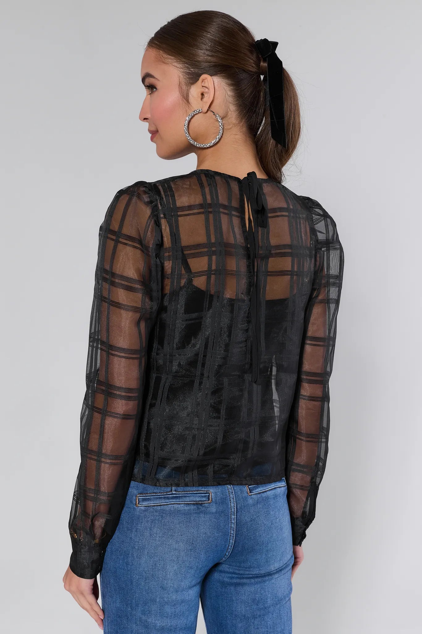 Woman wearing a black sheer long-sleeve Darcy top with plaid pattern on a white background