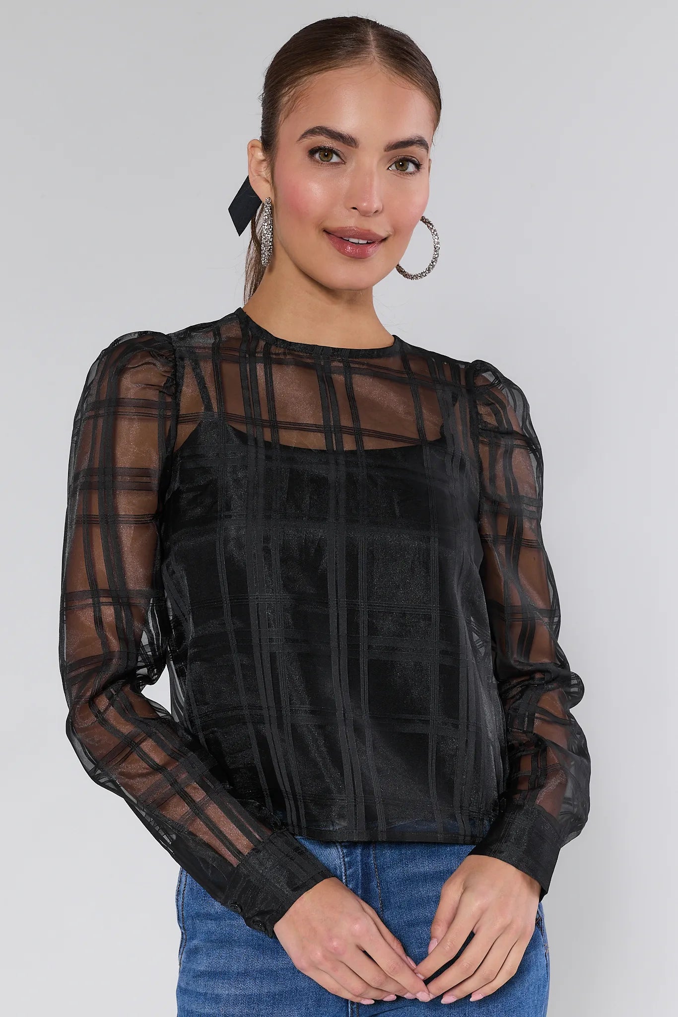 Woman wearing a black sheer long-sleeve Darcy top with plaid pattern on a white background