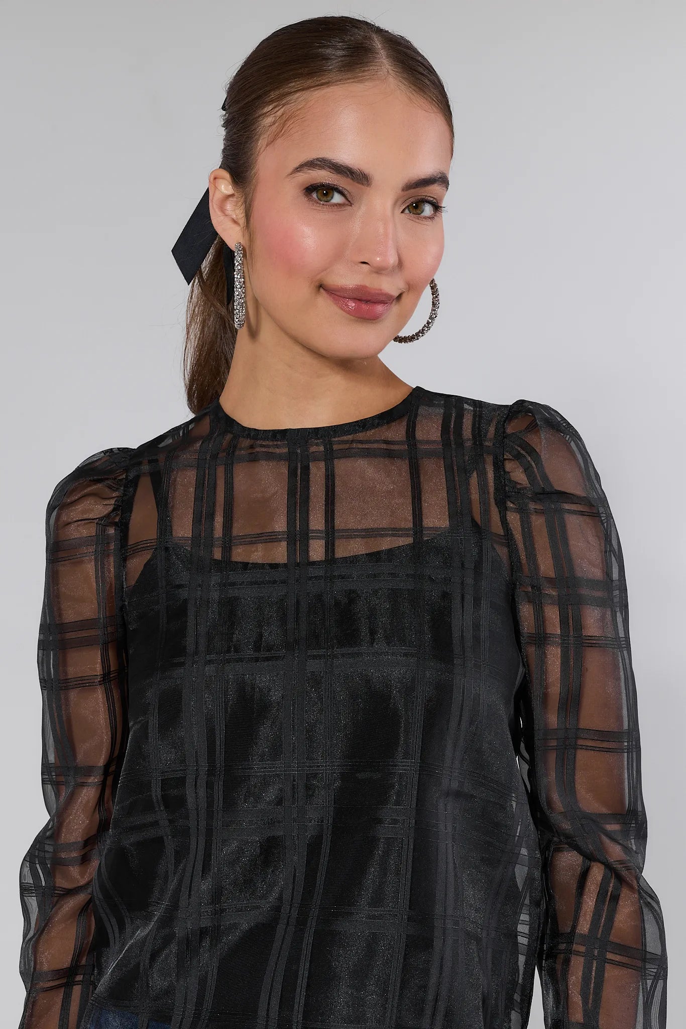 Woman wearing a black sheer long-sleeve Darcy top with plaid pattern on a white background