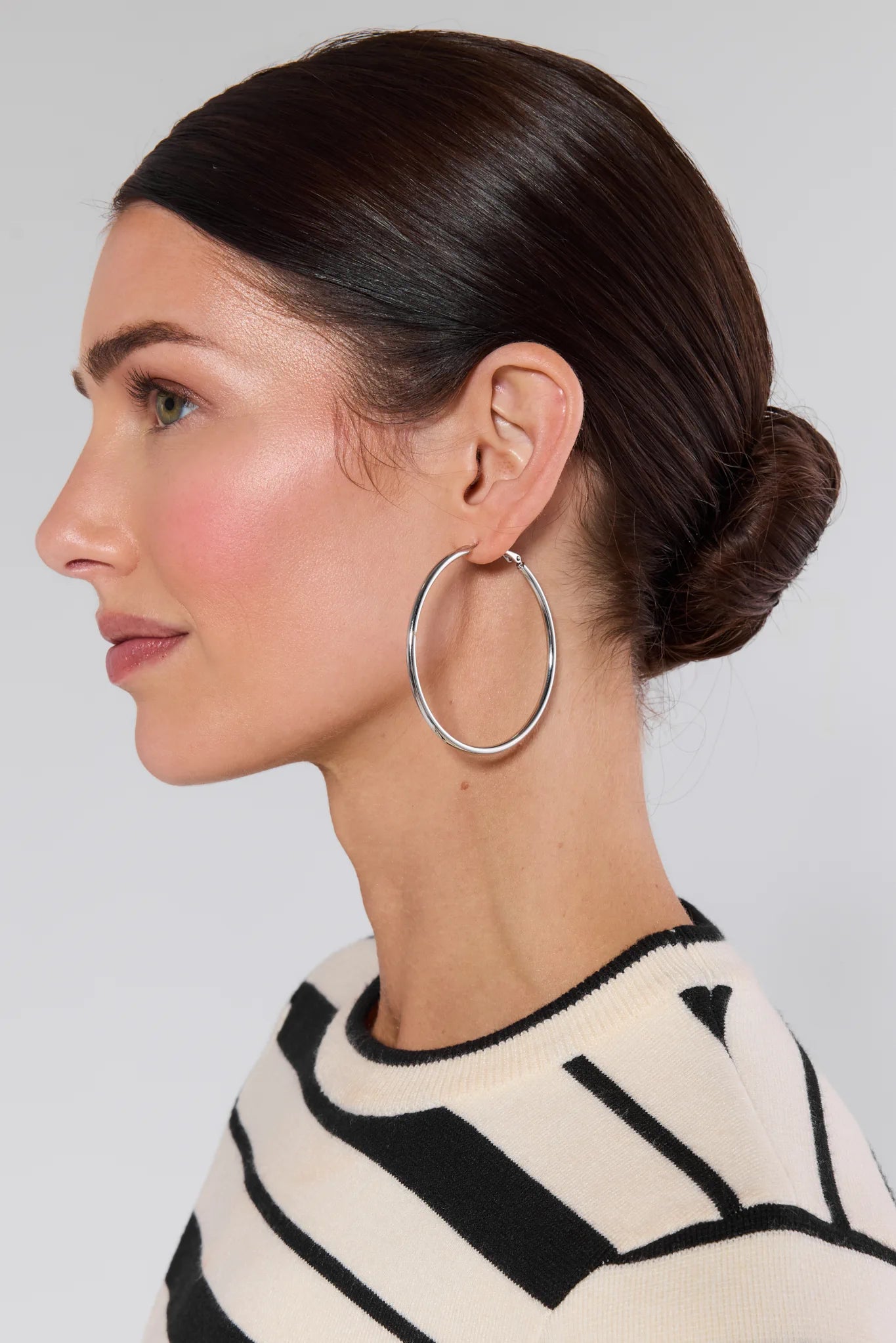 Woman wearing large hoop earrings with a neutral background