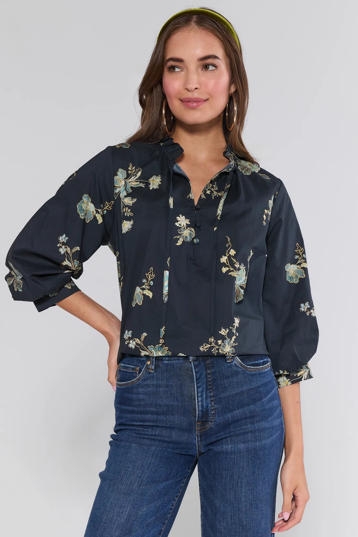 Woman wearing a dark floral Michelle Top and blue jeans against a white background