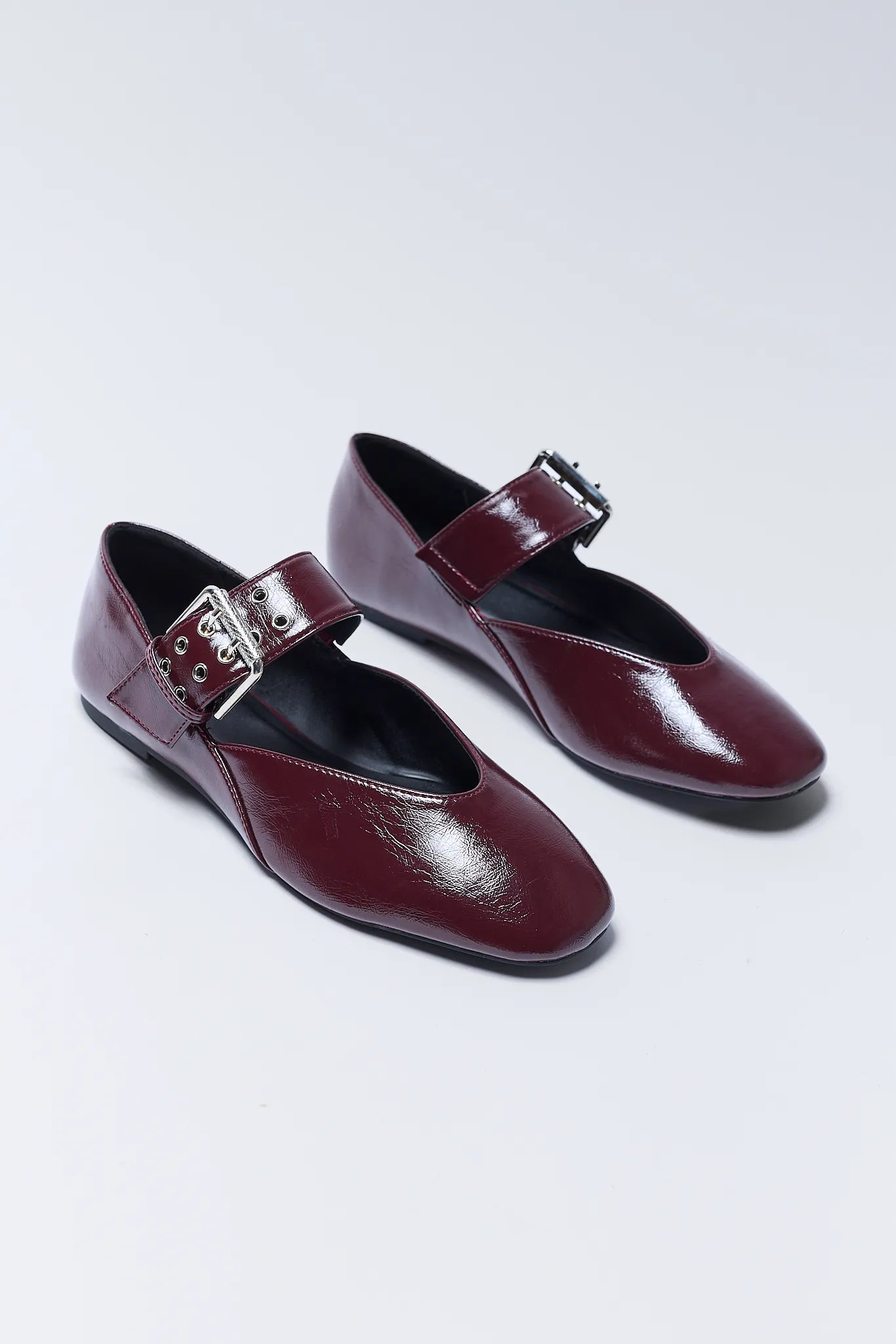Pair of burgundy Aspen Flats with buckles on a light gray background