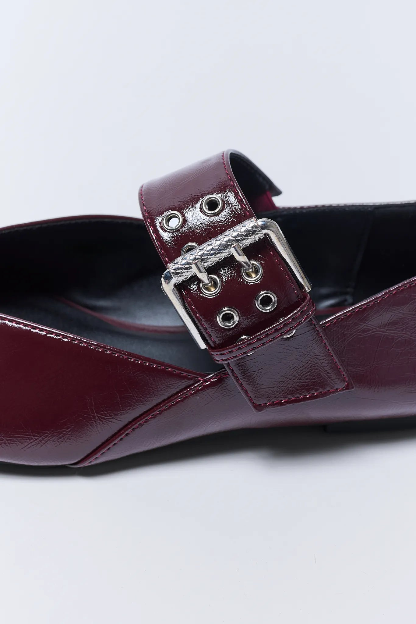 Close-up of a burgundy Aspen Flats with a silver buckle on a white background