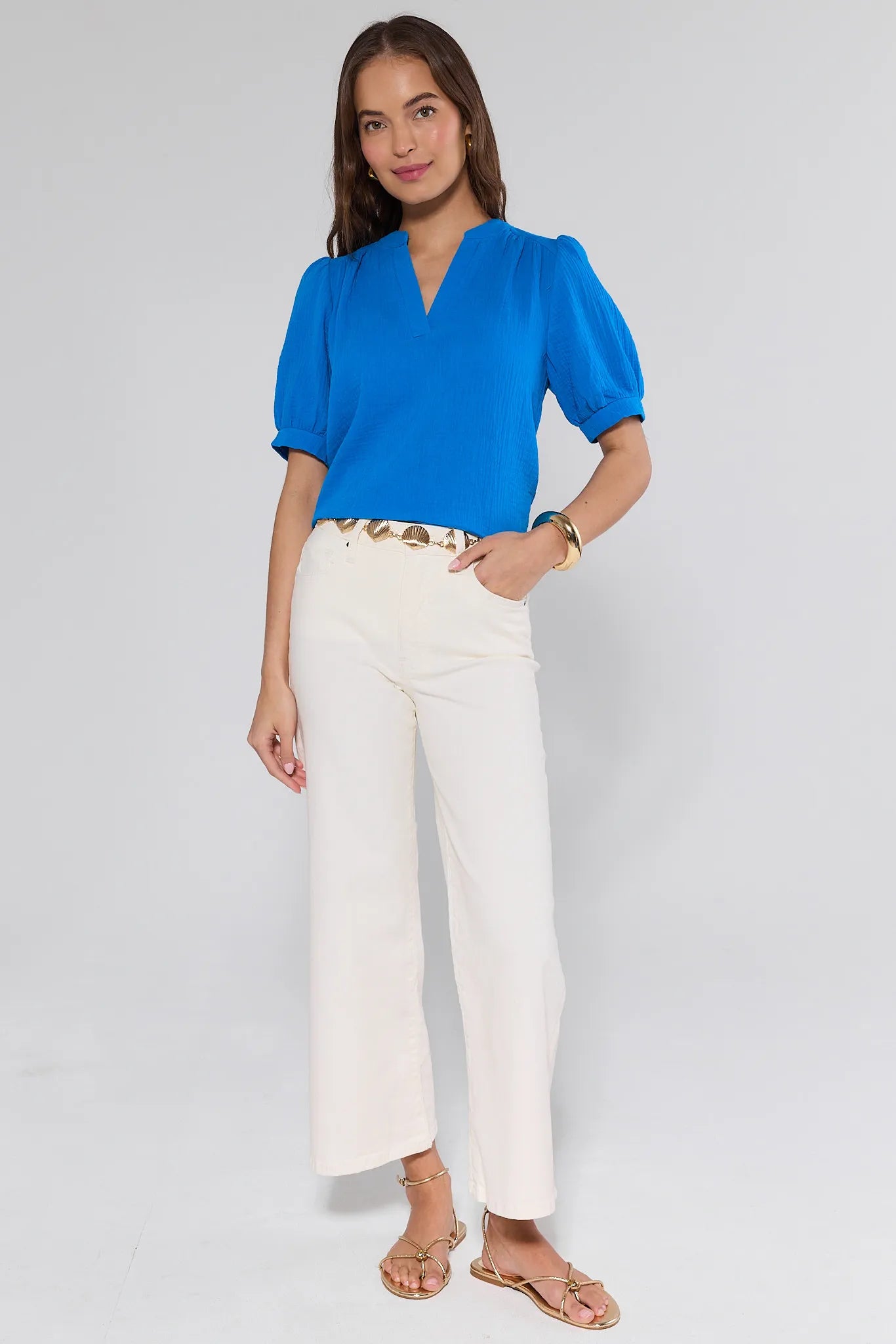 Woman wearing a blue blouse and white pants on a gray background