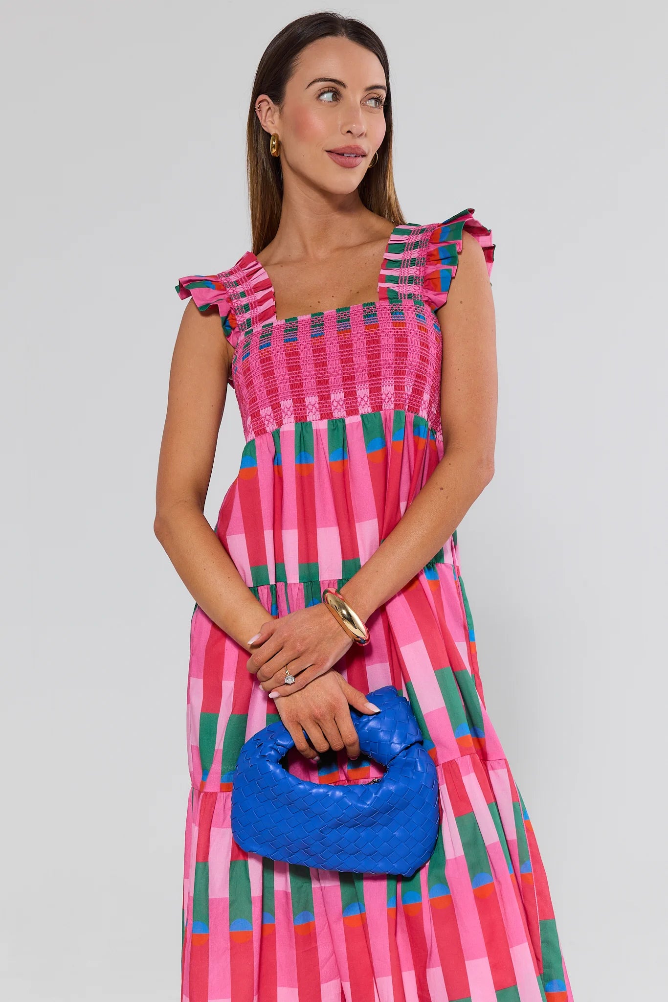 Woman wearing a colorful dress holding a blue handbag against a plain background