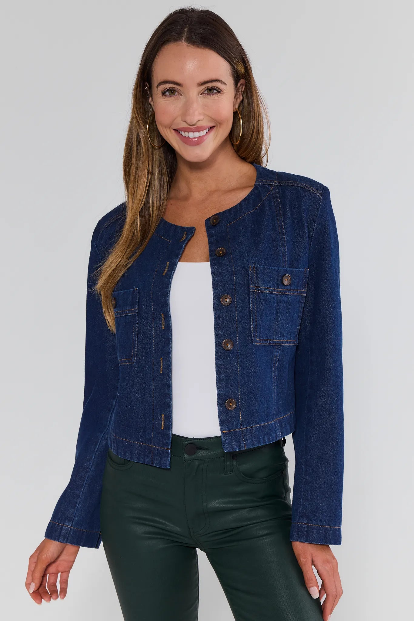 Woman wearing a blue denim Vera Jacket over a white top and green pants on a plain background