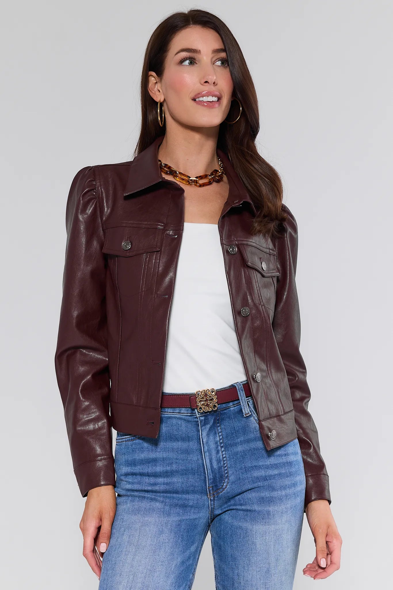 Woman wearing a brown Roxanna Leather Jacket, white top, and blue jeans on a plain background