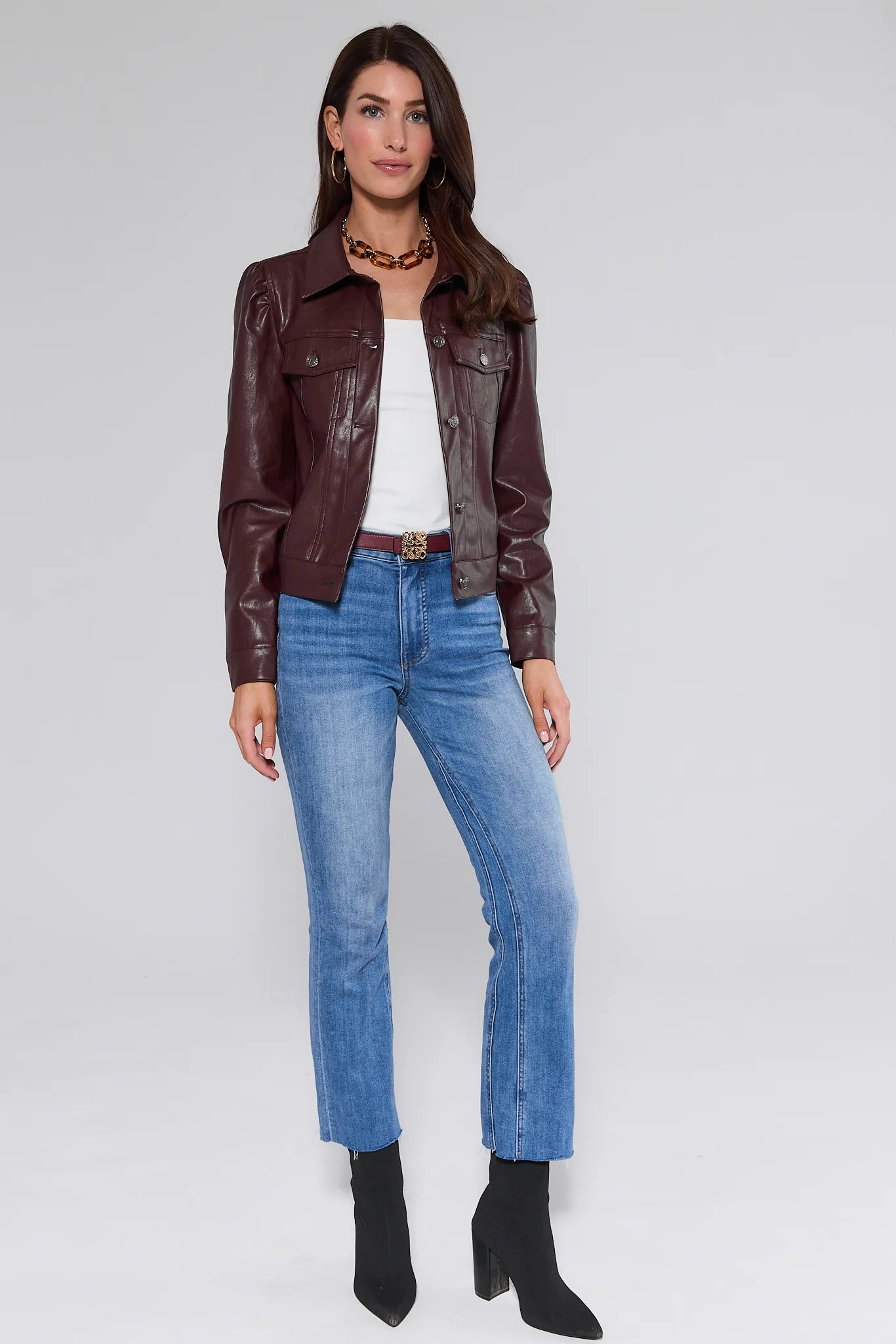 Woman wearing a brown Roxanna Leather Jacket, white top, blue jeans, and black boots on a white background