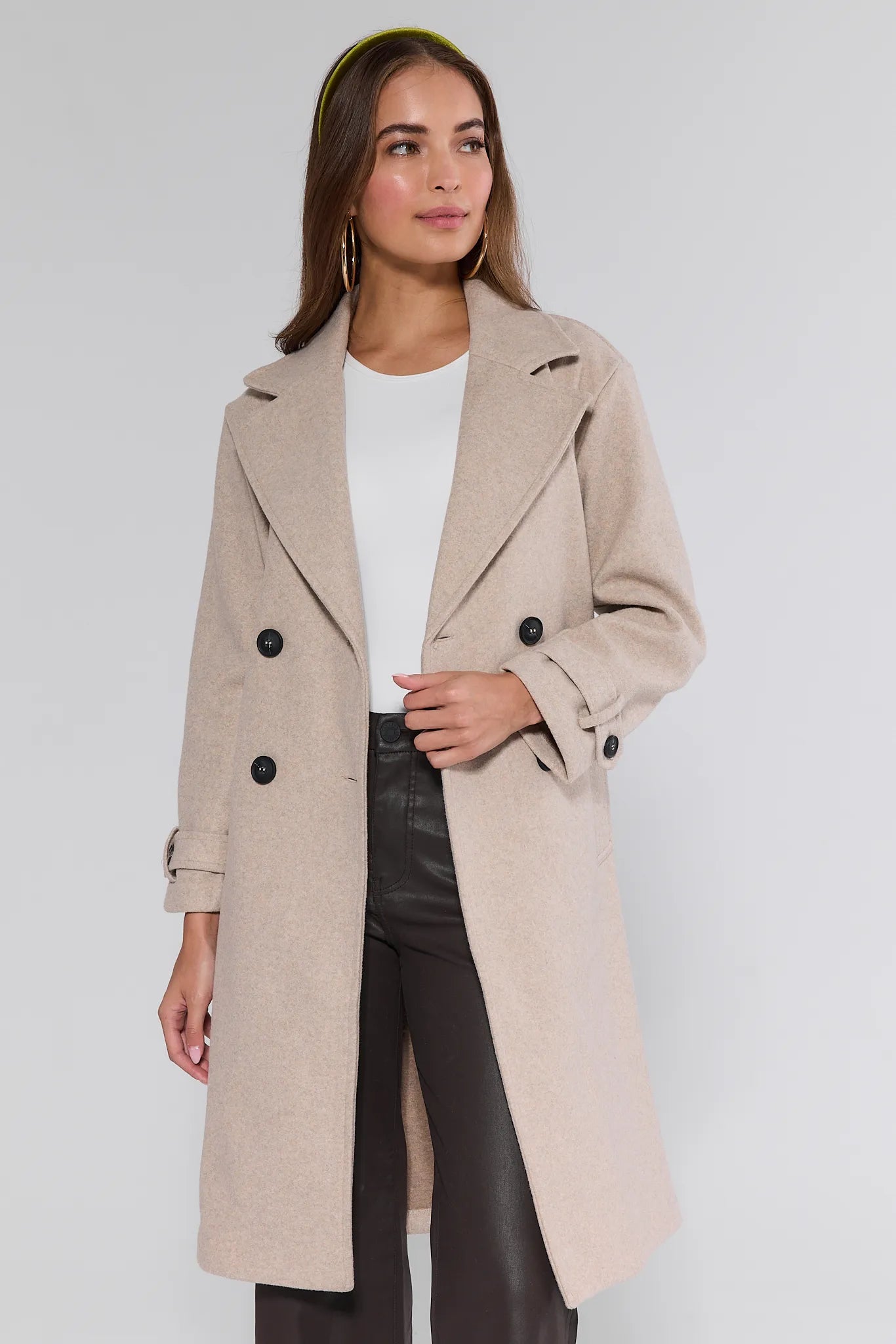 Woman wearing a beige Sadie Coat with black buttons on a white background