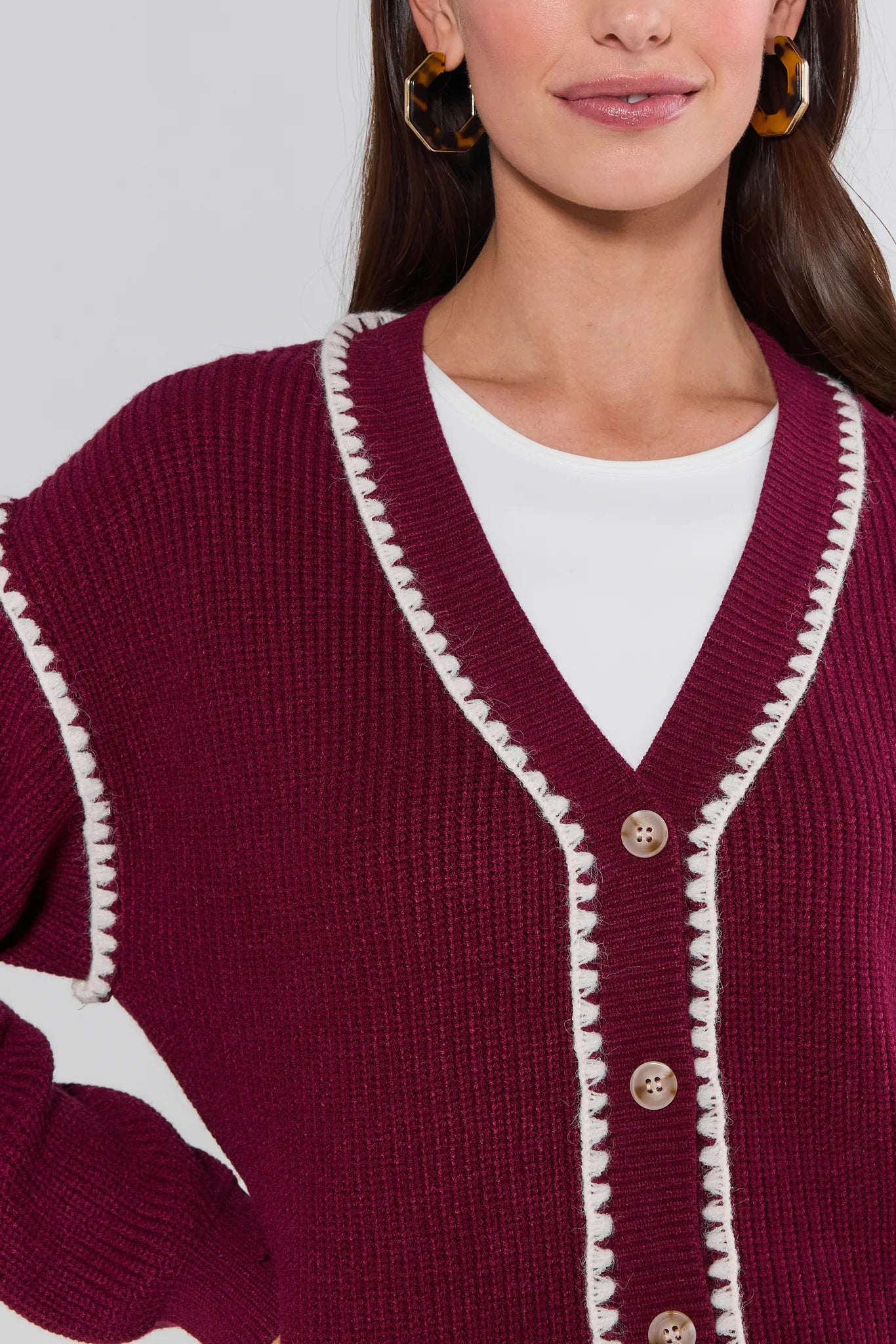 Close-up of a person wearing a burgundy Morgan Cardigan with white trim and buttons.