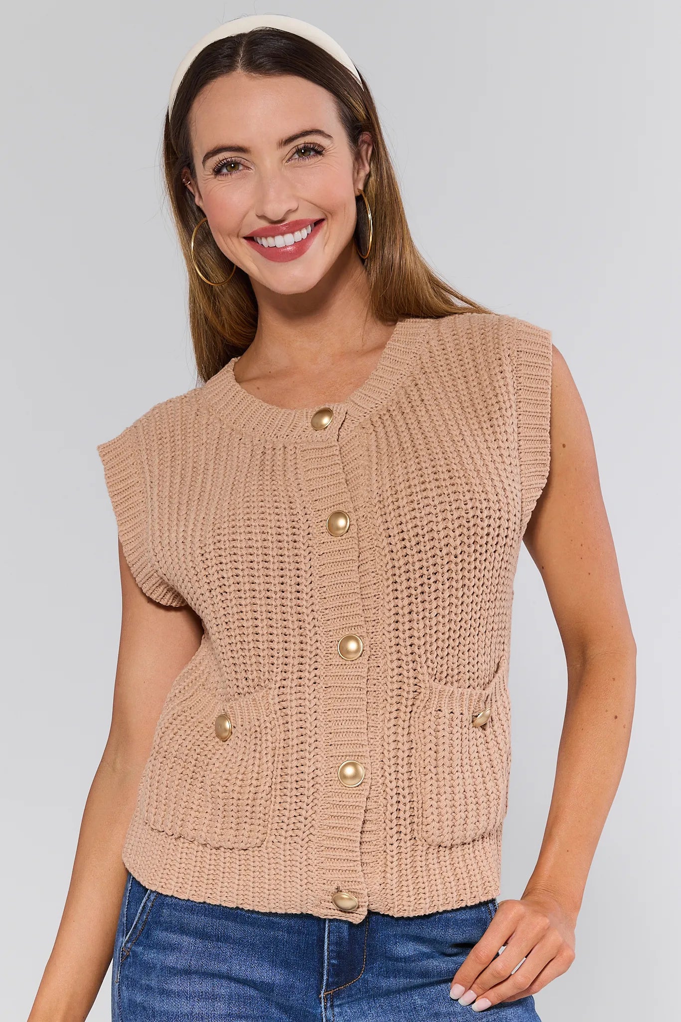 Woman wearing a beige knitted Angelina Vest with gold buttons on a plain background