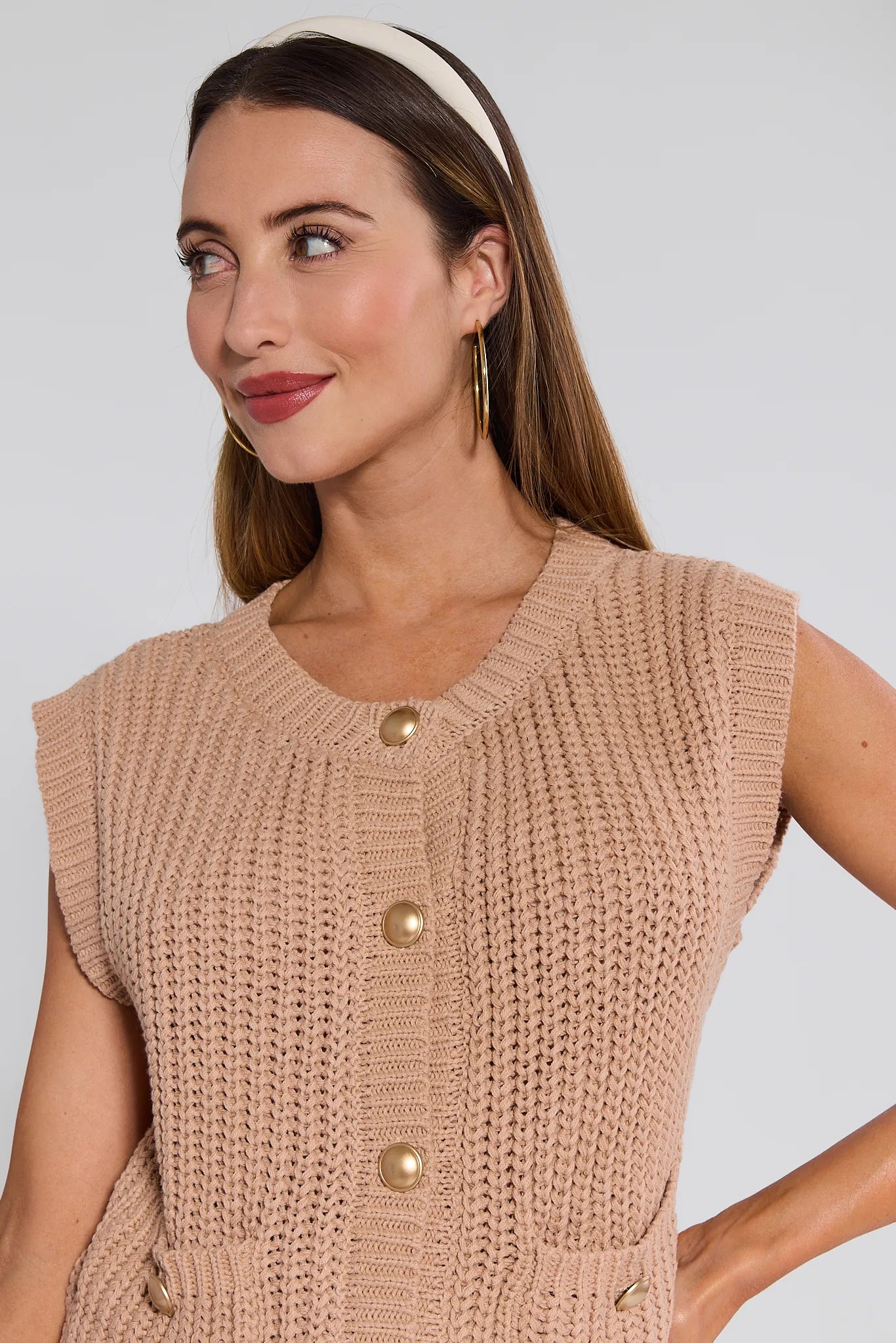 Woman wearing a beige knitted Angelina Vest with buttons on a plain background