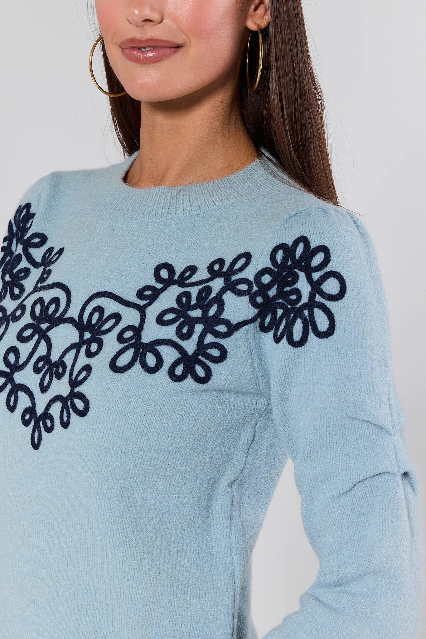 Woman wearing a Natasha Blue Embroidered Sweater with black embroidery on a plain background