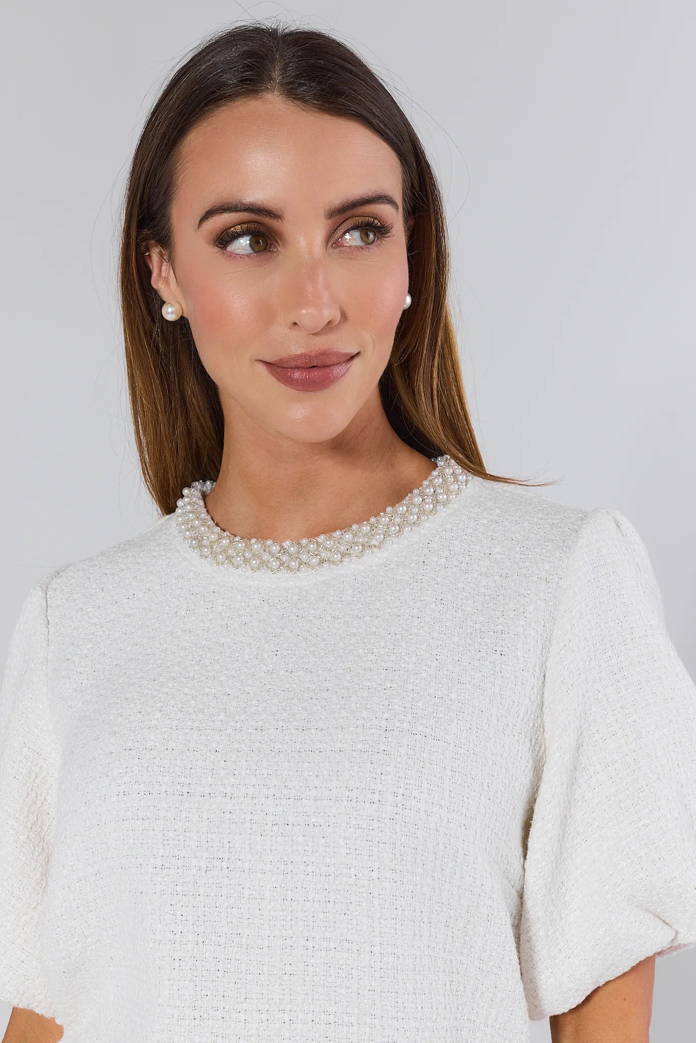 Woman wearing a white Blakely Top with pearl details against a plain 