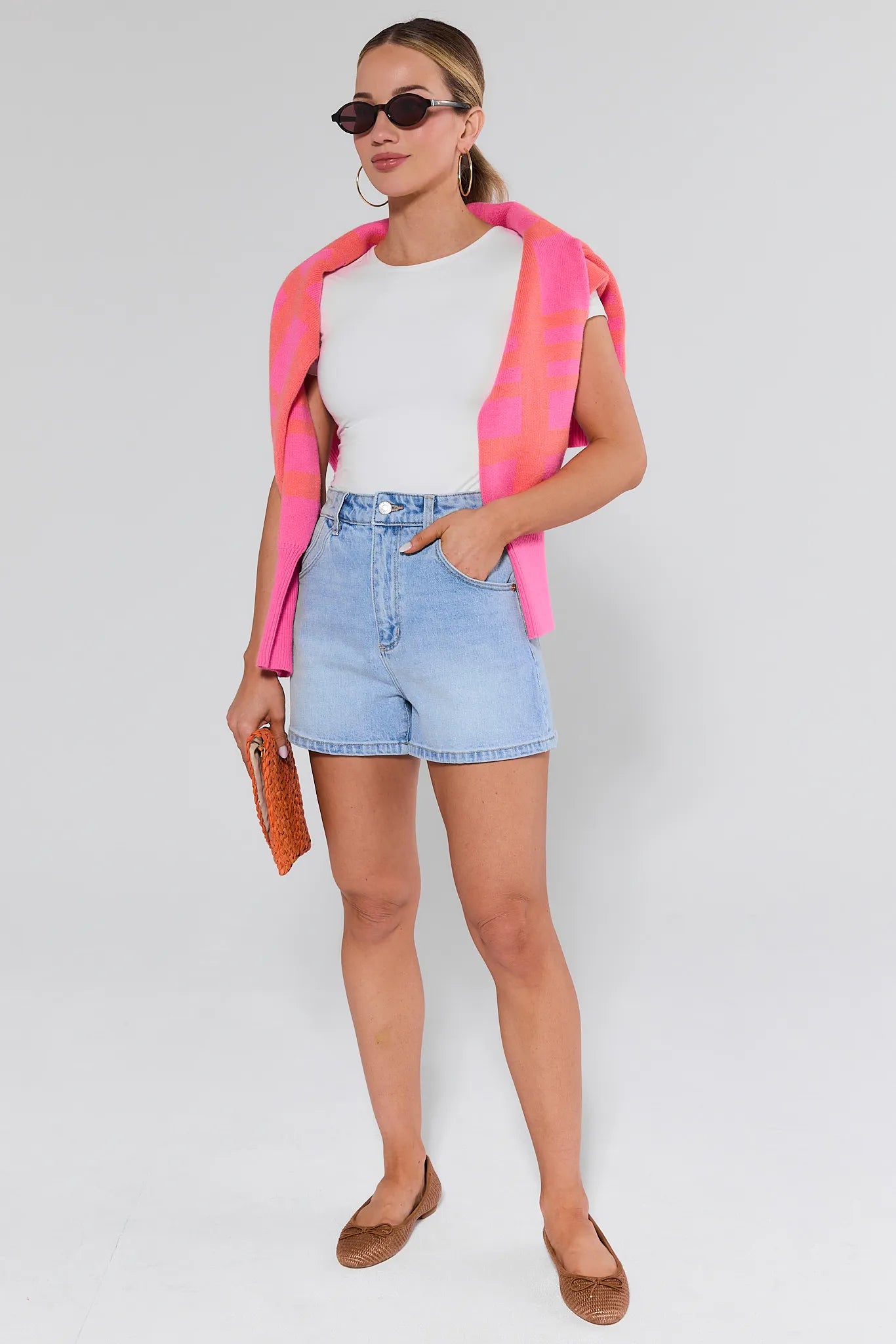 Woman wearing a pink and red jacket, white shirt, blue shorts, and brown shoes on a white background