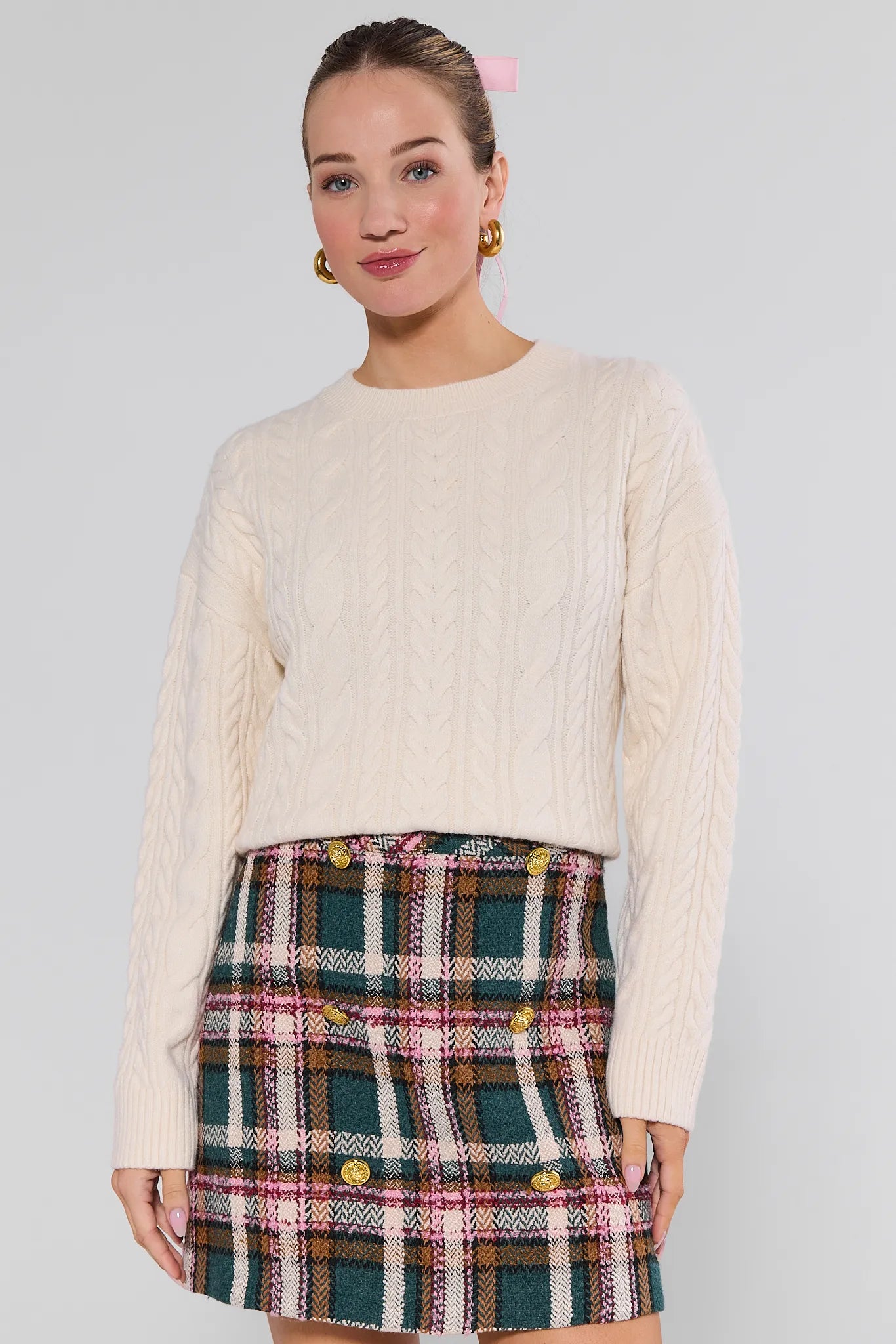 Woman wearing a cream Dakota Sweater and plaid skirt against a plain background
