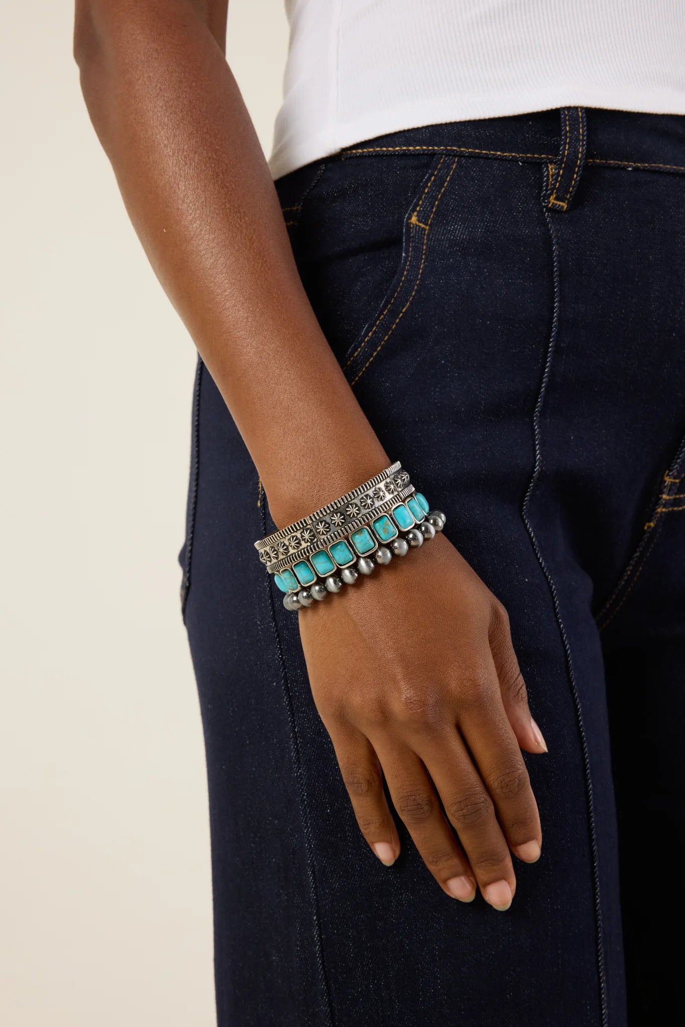 Hand wearing multiple bracelets with a neutral background
