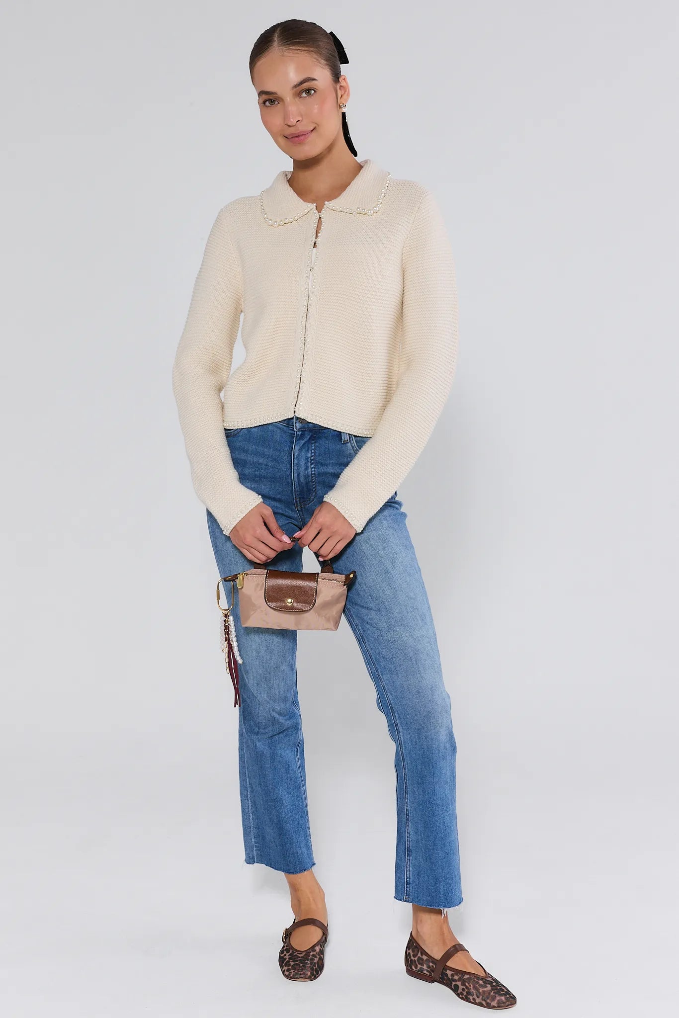 Woman wearing a cream-colored teagan cardigan and blue jeans on a plain background