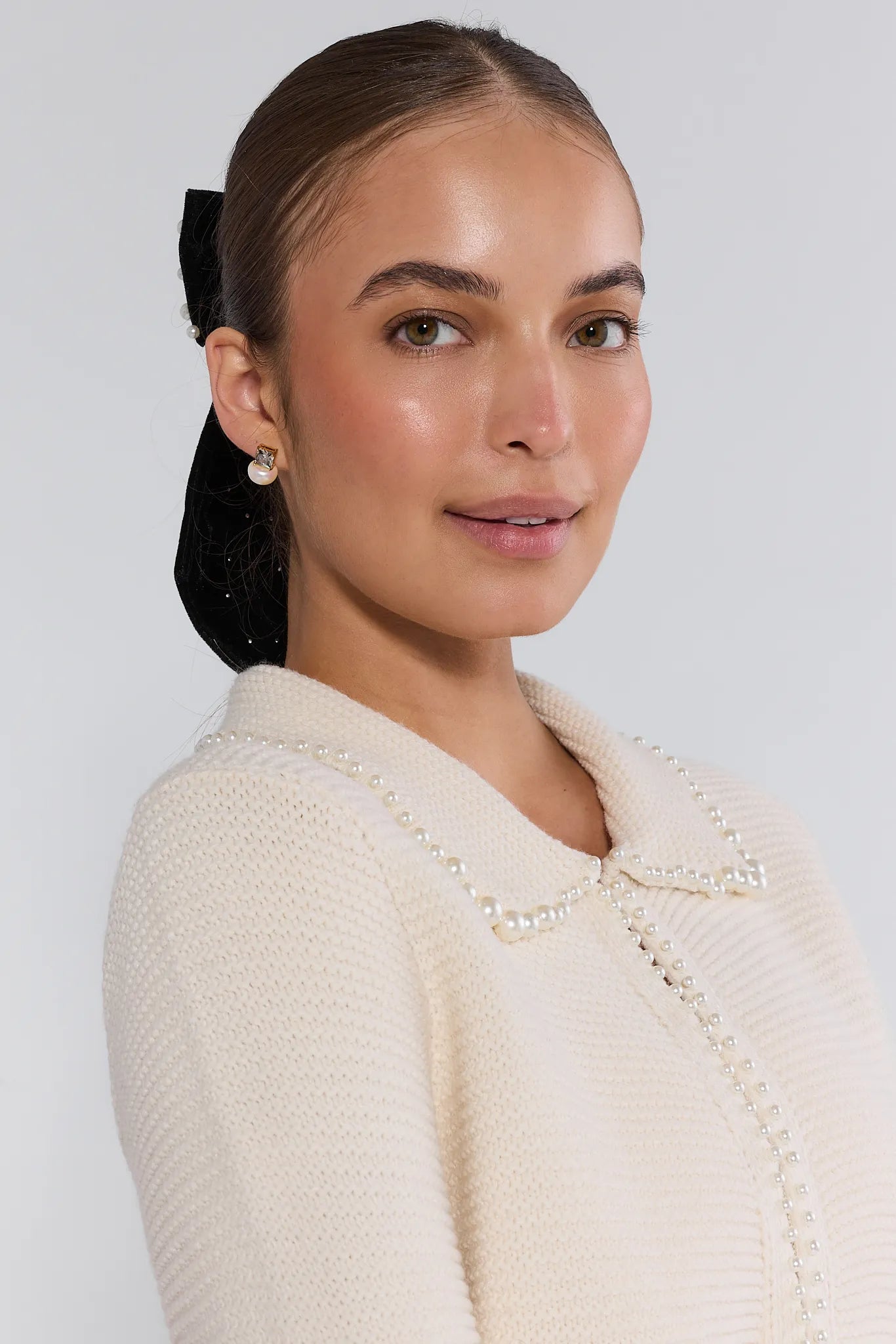 Woman wearing a cream-colored teagan cardigan and blue jeans on a plain background