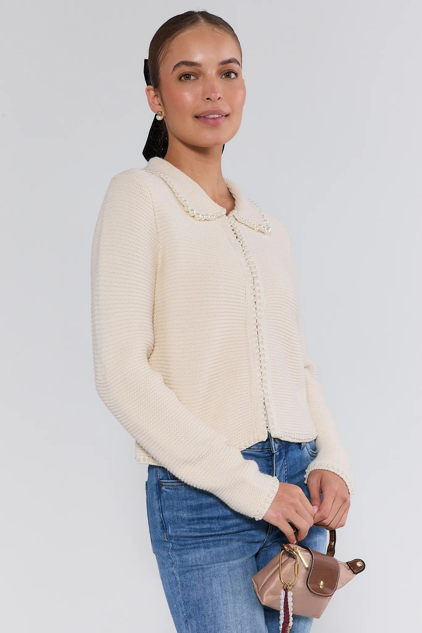 Woman wearing a cream-colored teagan cardigan and blue jeans on a plain background