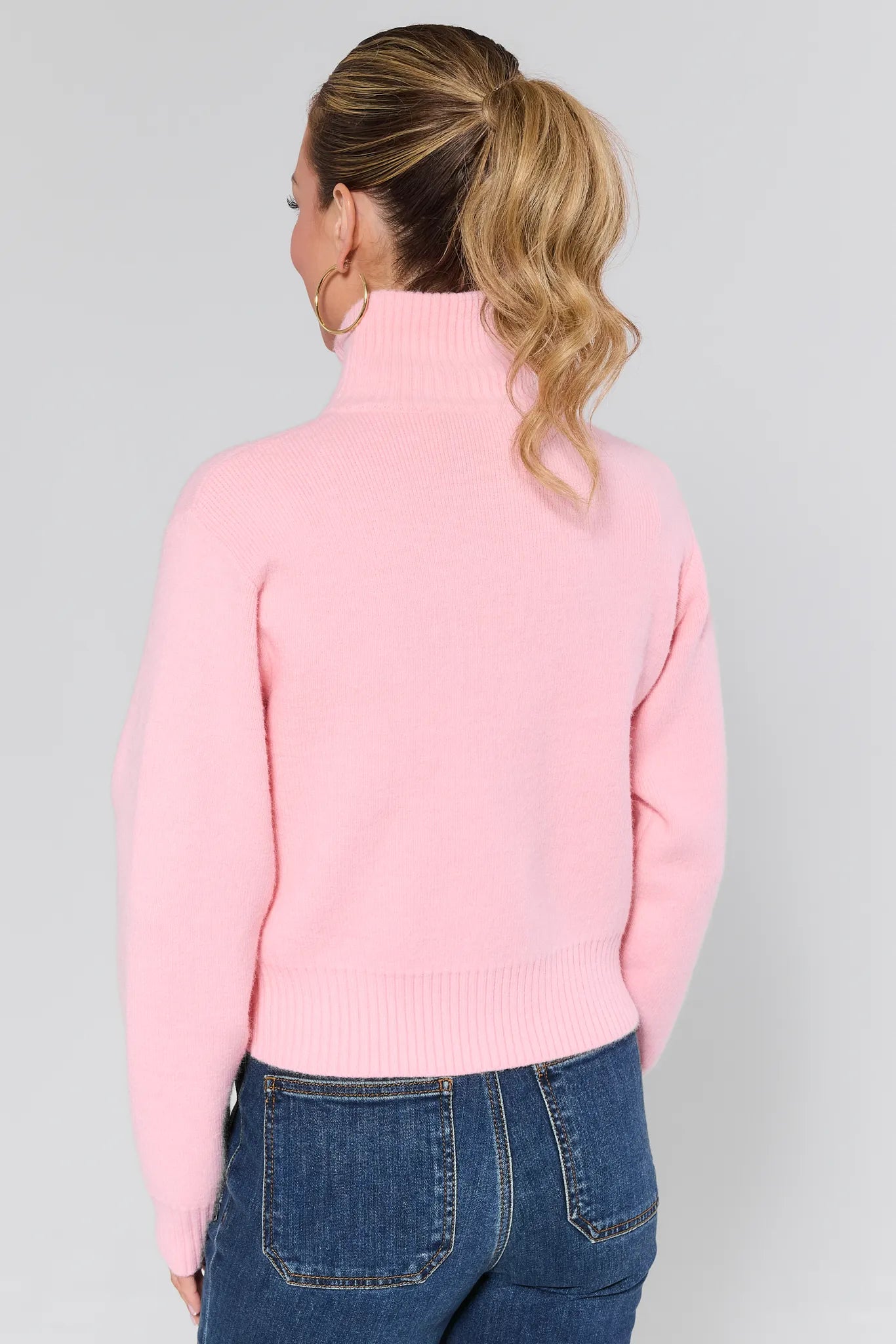 Woman wearing a Brighton Sweater over a white top and blue jeans on a plain background