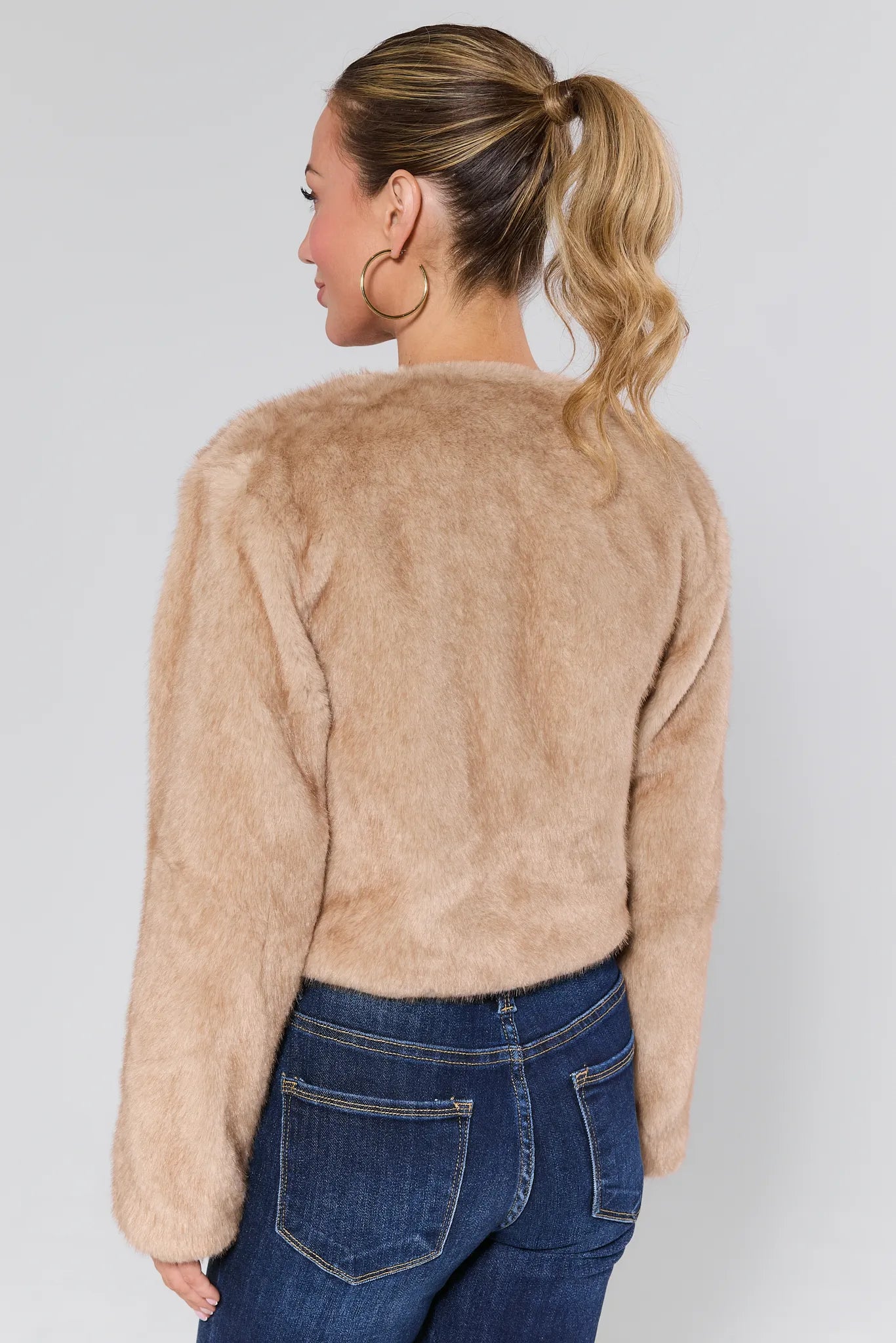 Woman wearing a Tamara Ivory Faux Fur Jacket and blue jeans on a white background